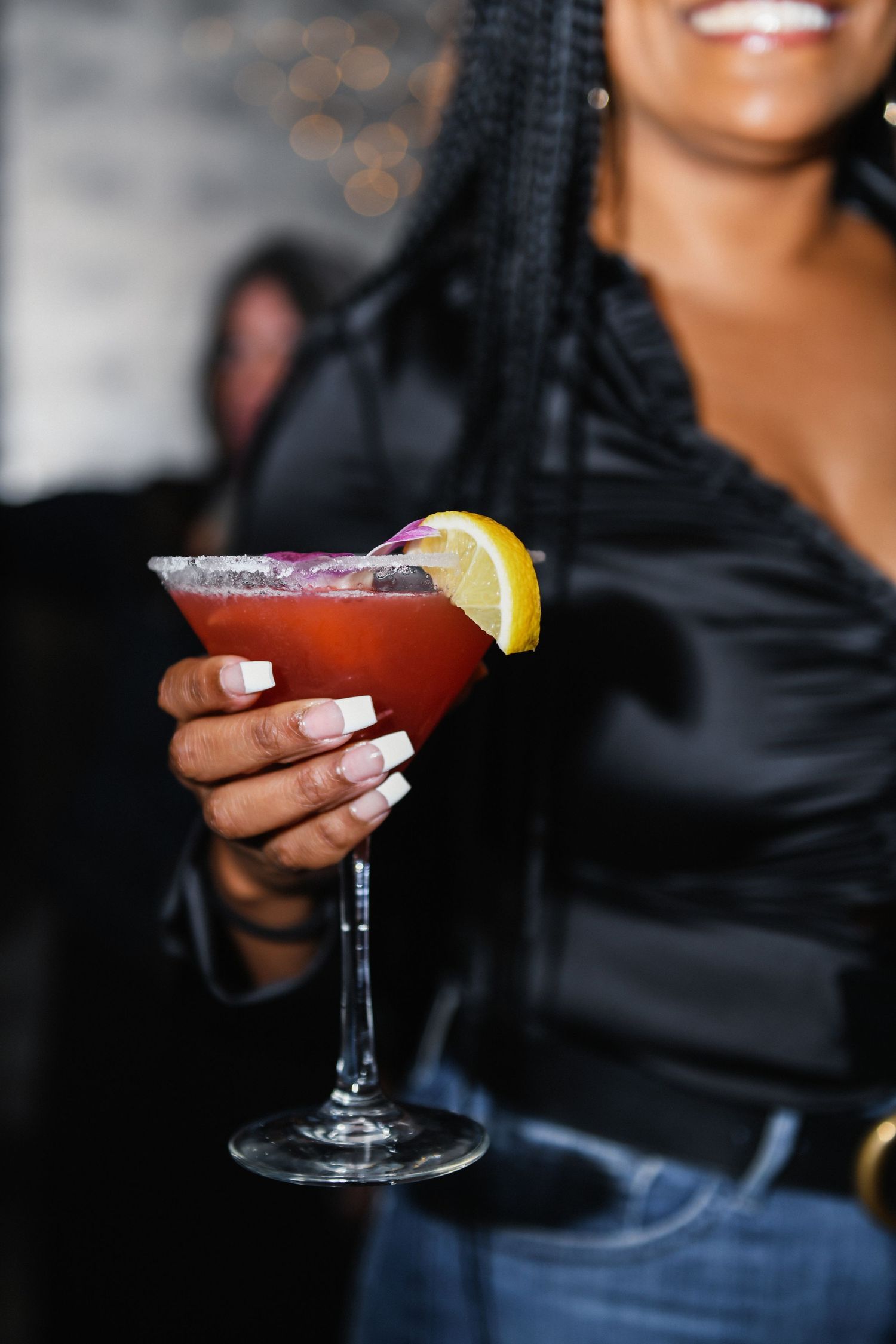 Hand holding a red cocktail garnished with lemon in a martini glass.