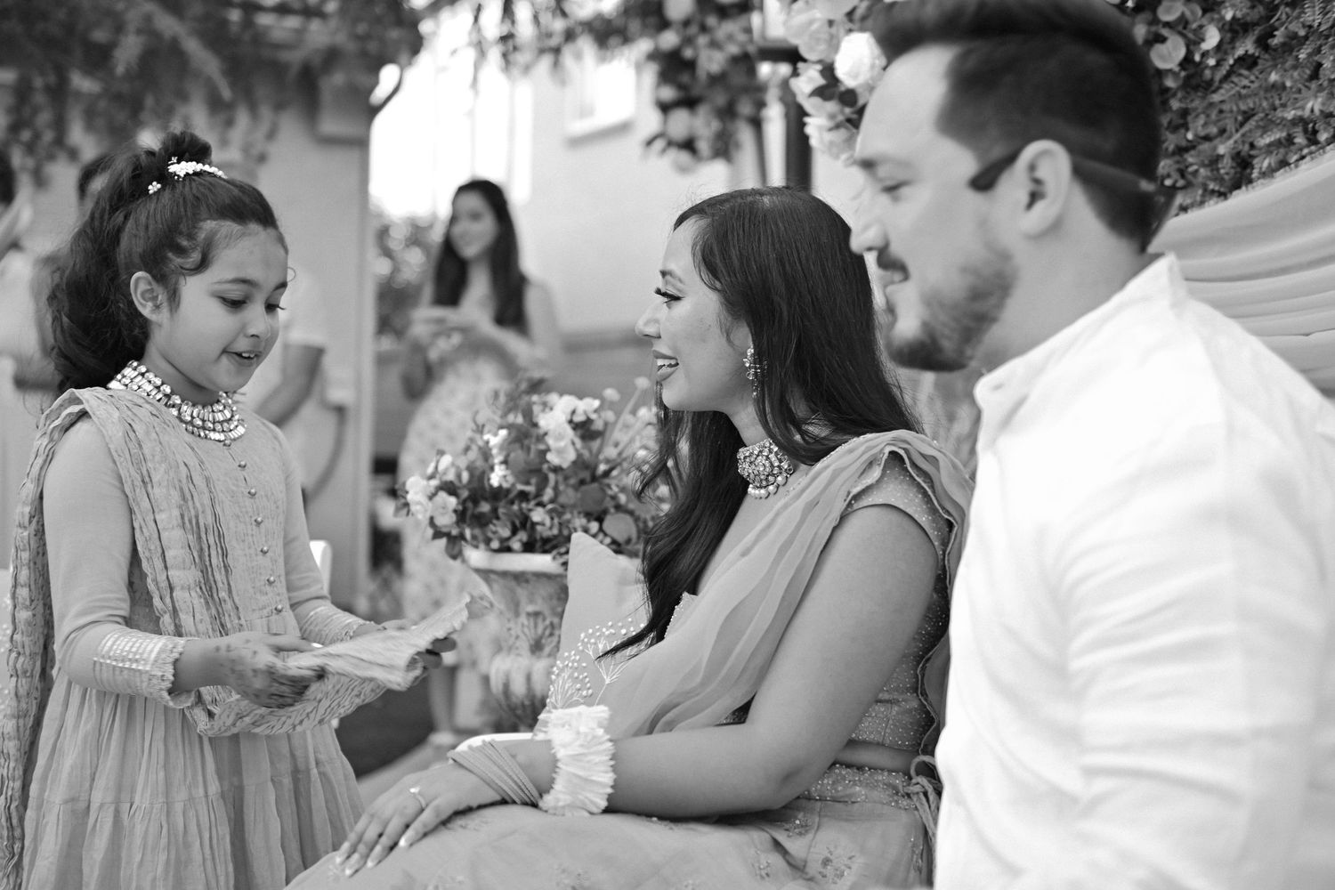 Black and white candid photo of outdoor gathering with floral arrangements.