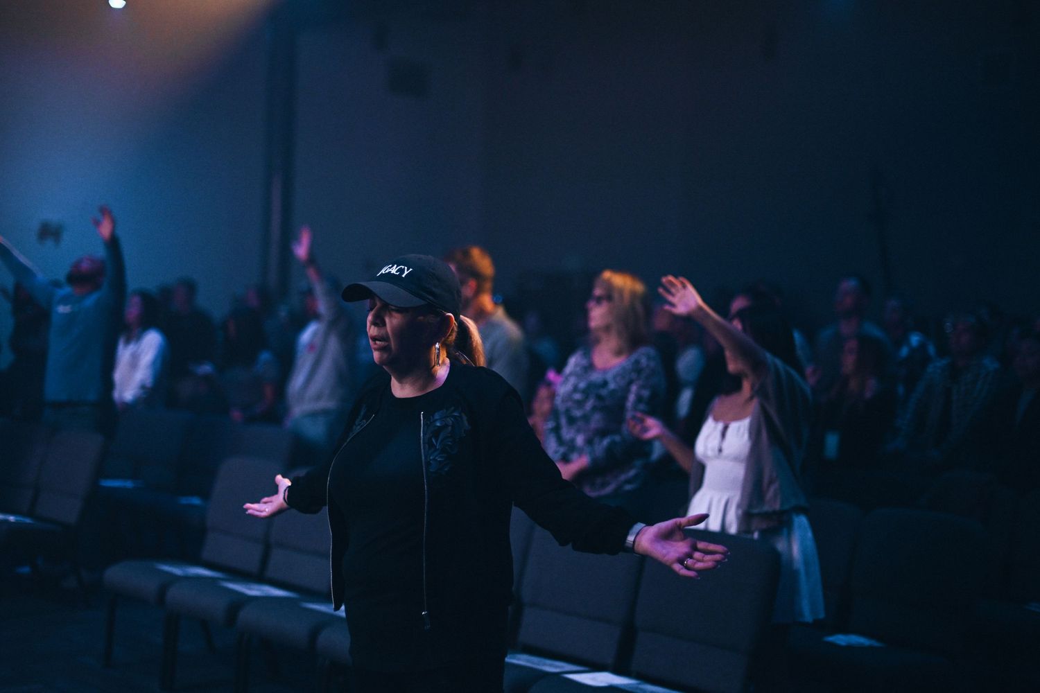 Crowd of worship attendees raise their hands during an atmospheric church service.