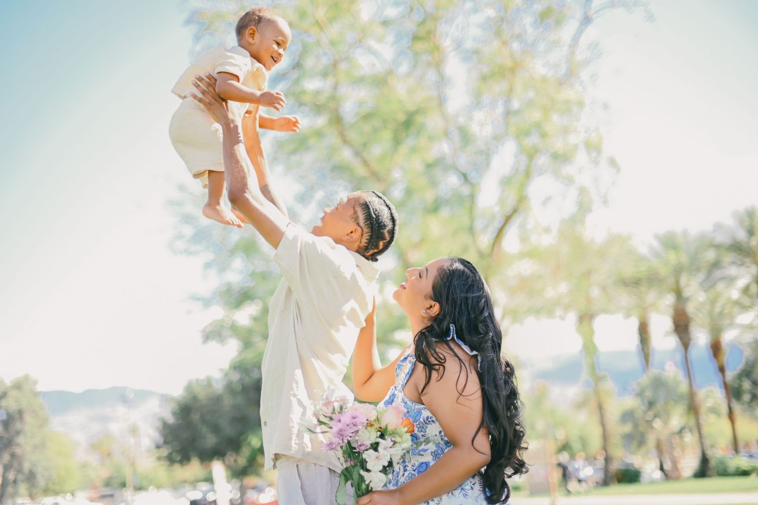 Joyful outdoor family moment with lifted child against nature backdrop.