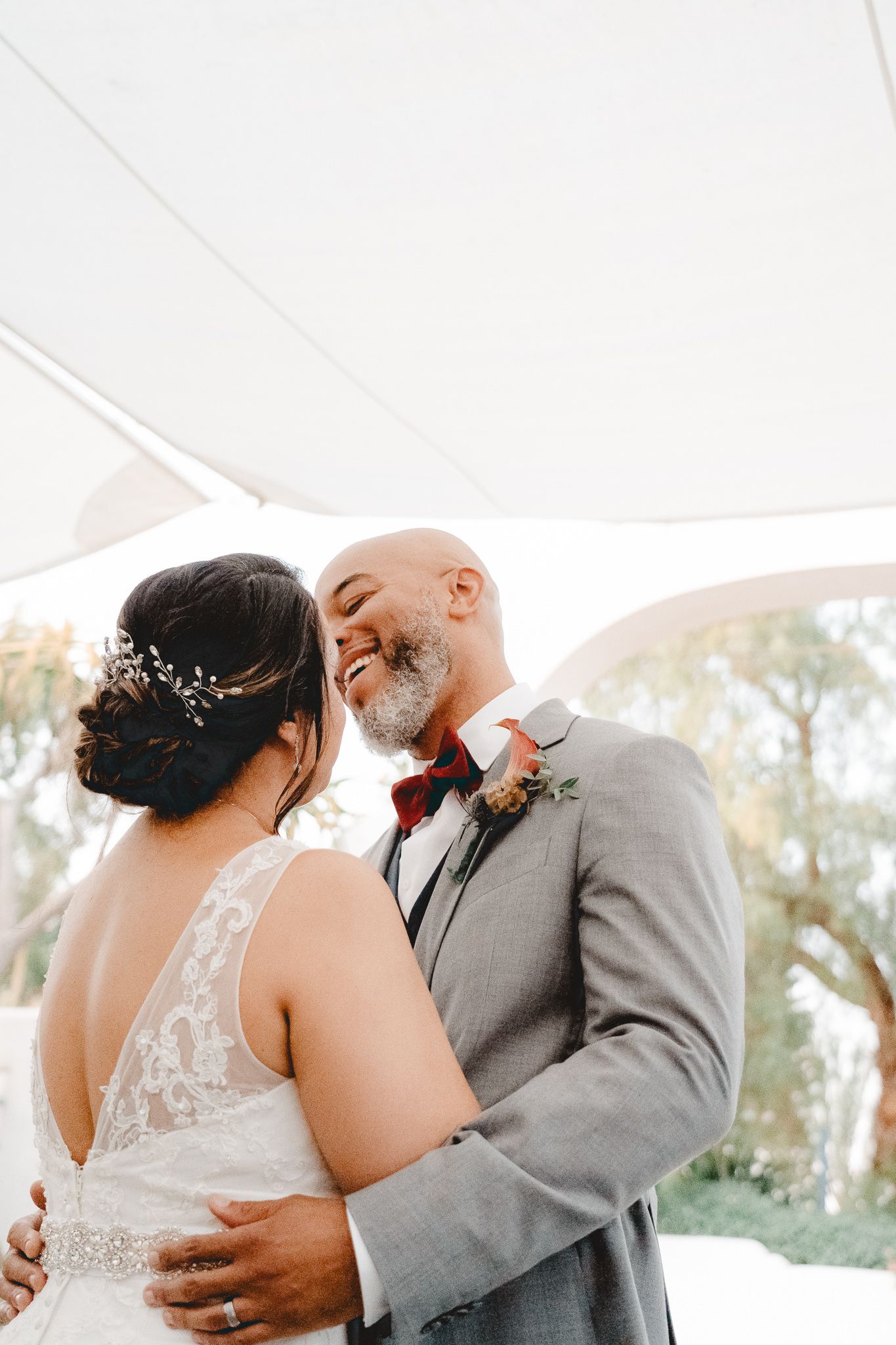 A tender moment between newlyweds during their wedding ceremony under a white canopy.