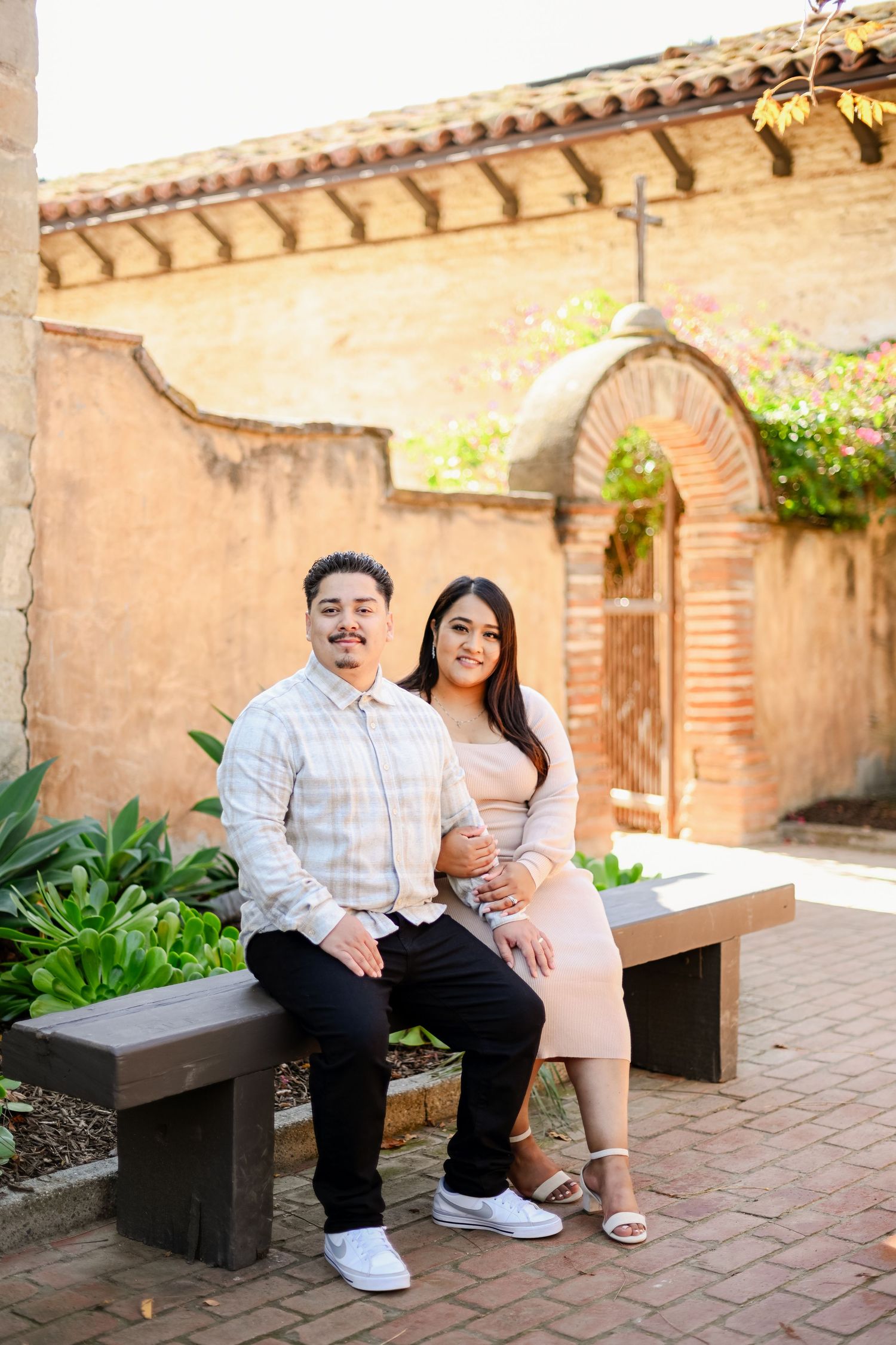 A couple sitting on a stone bench in a Spanish-style courtyard with arched doorways.