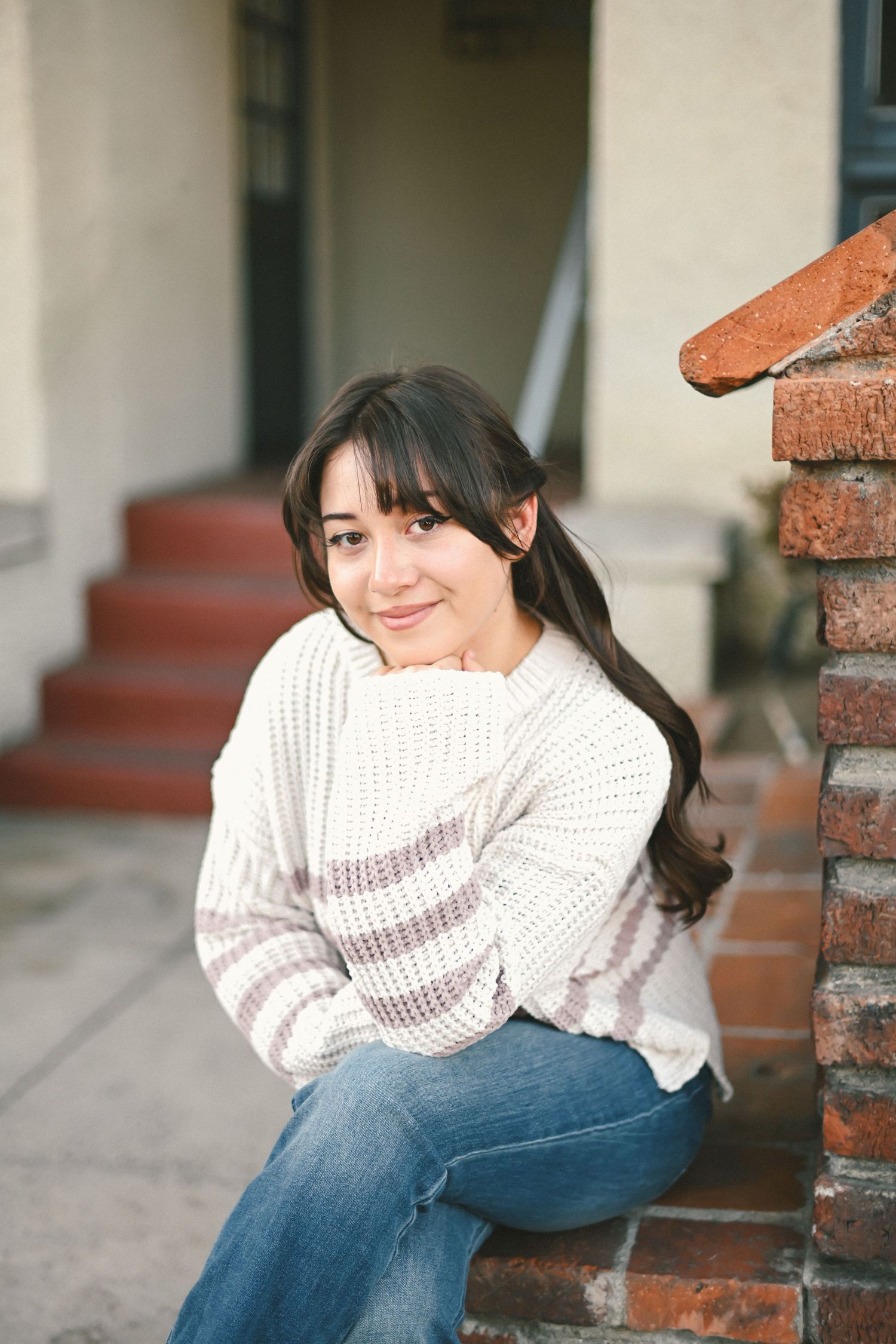 A cozy winter portrait with someone wearing a cream knit sweater sitting on brick steps.