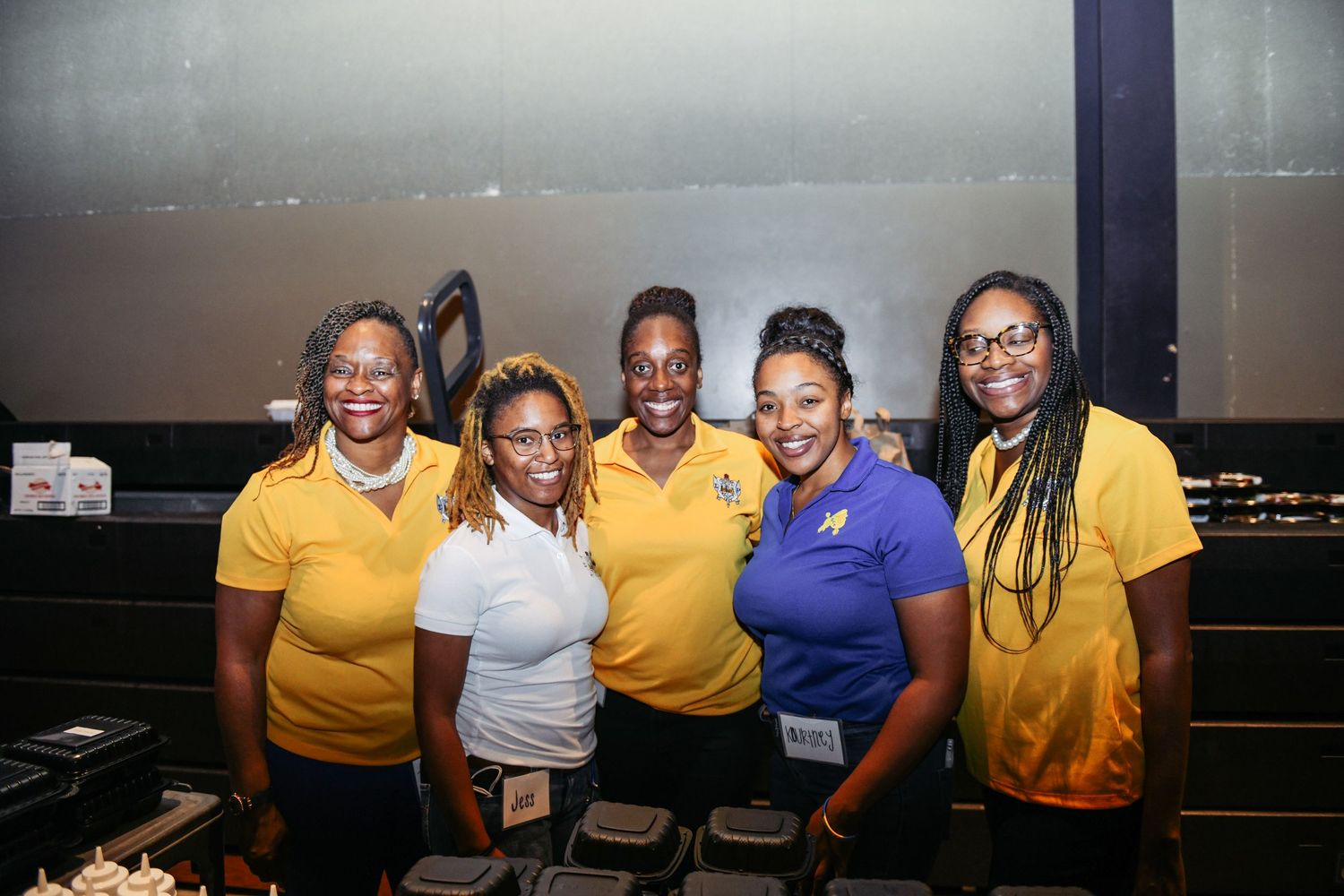 Group of staff members in yellow and blue uniforms smiling together at an event.