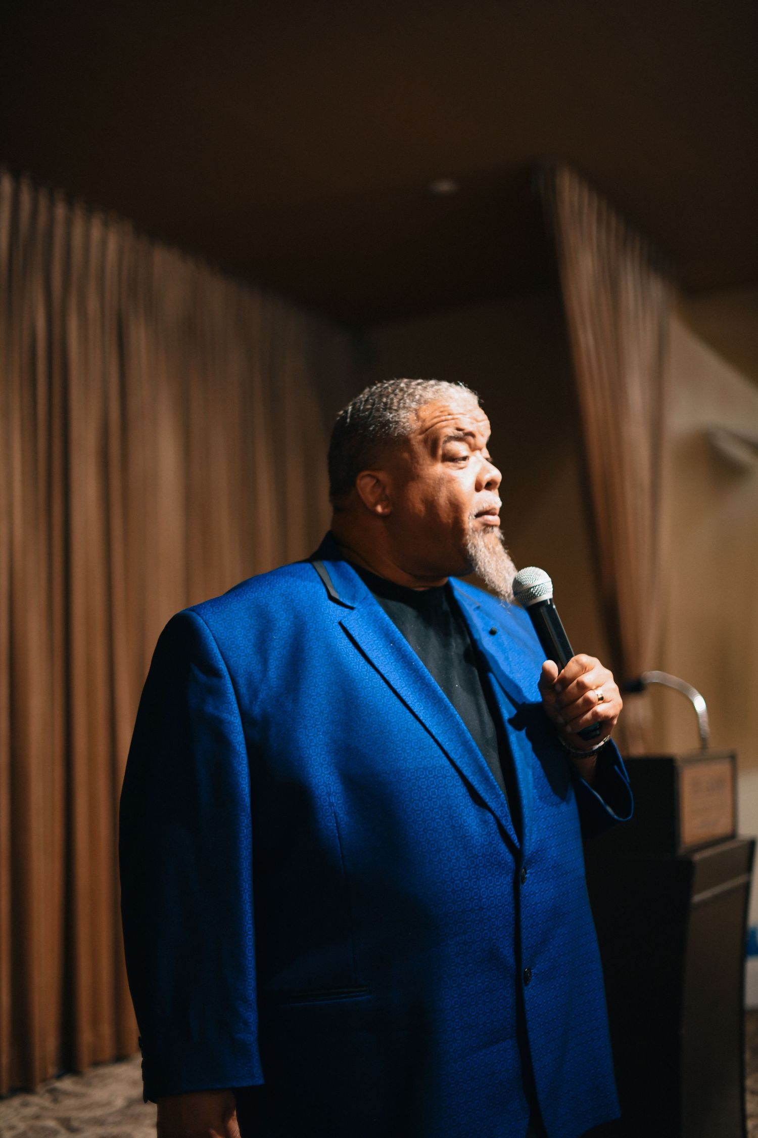 Speaker in bright blue suit jacket performing on stage with microphone.