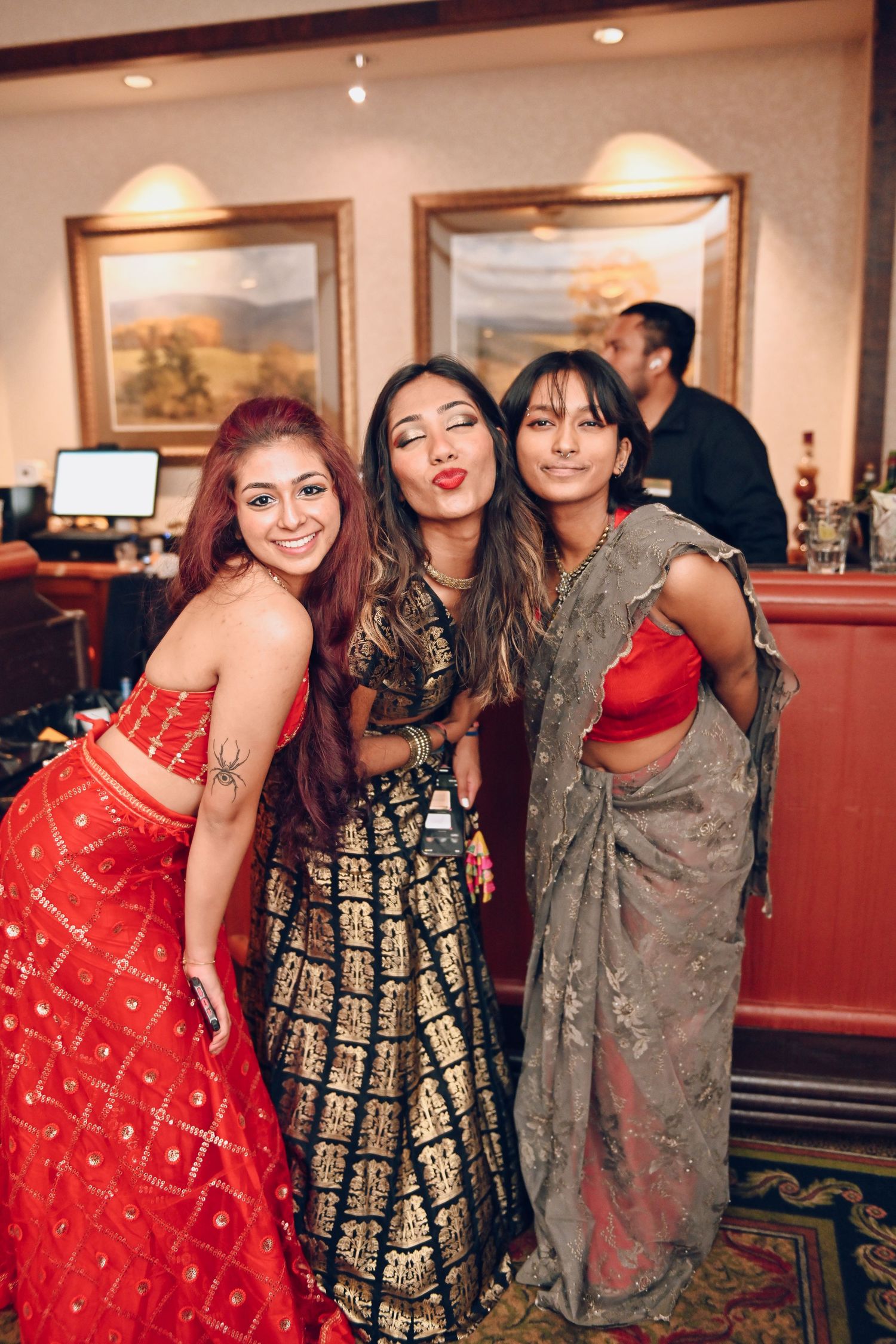 Three friends in traditional Indian formal wear pose together at reception.