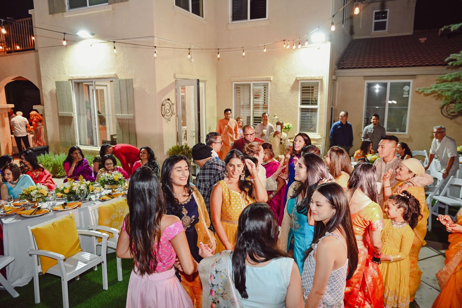 Colorful evening reception party with guests dancing under string lights.