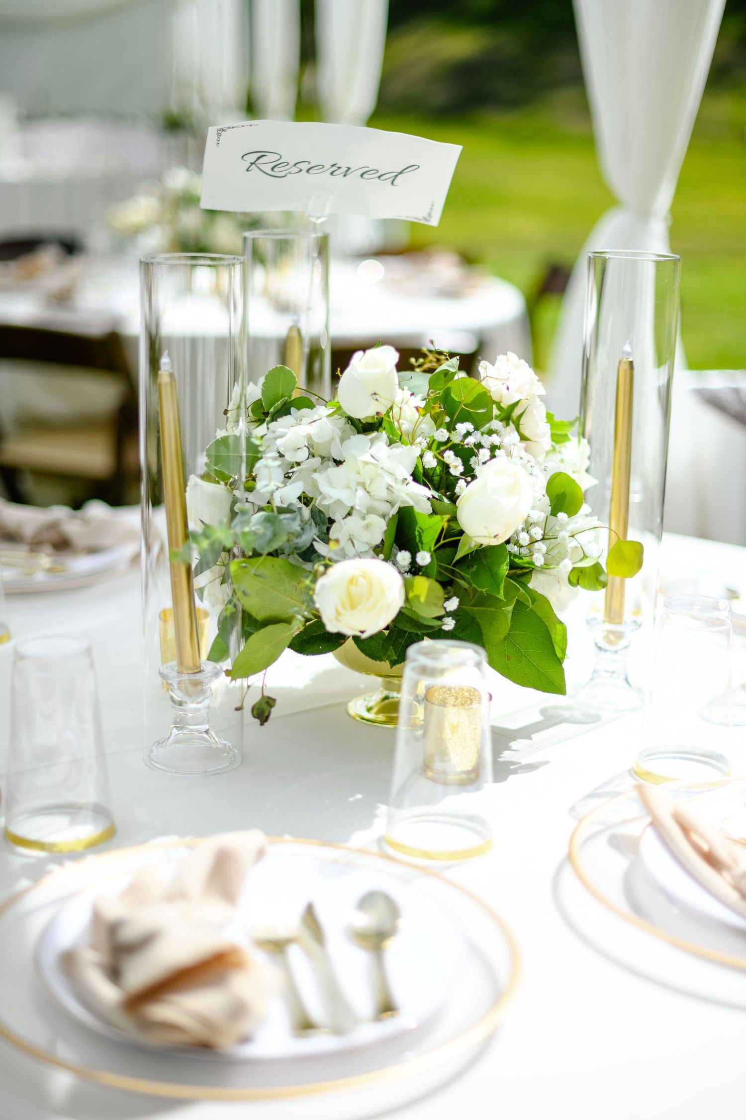 Elegant white floral centerpiece with reserved sign on wedding reception table.