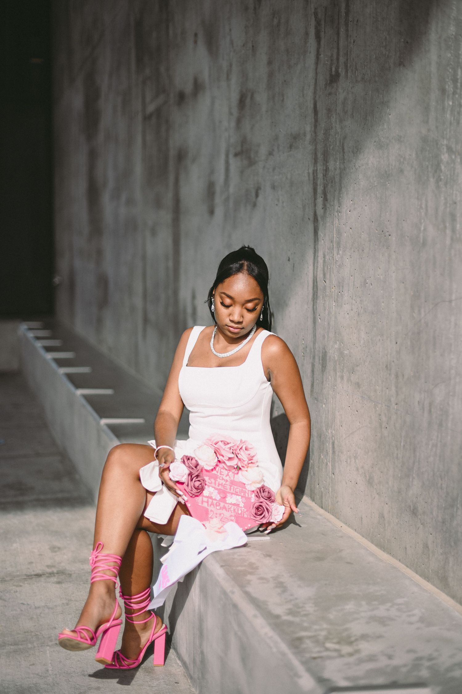 Fashion portrait of person in white dress with pink accessories sitting on concrete ledge.