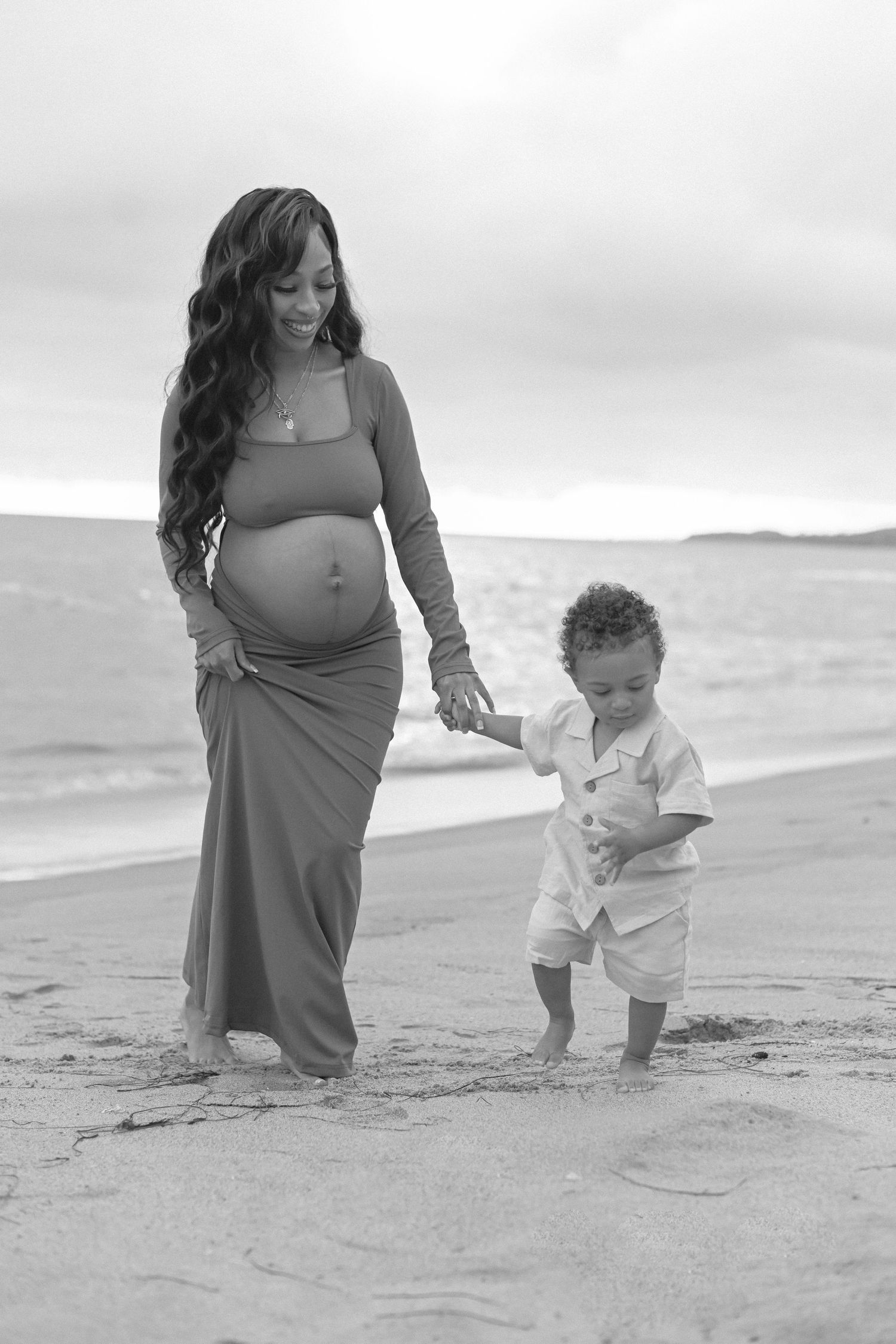 Black and white portrait of mother and child walking on beach.