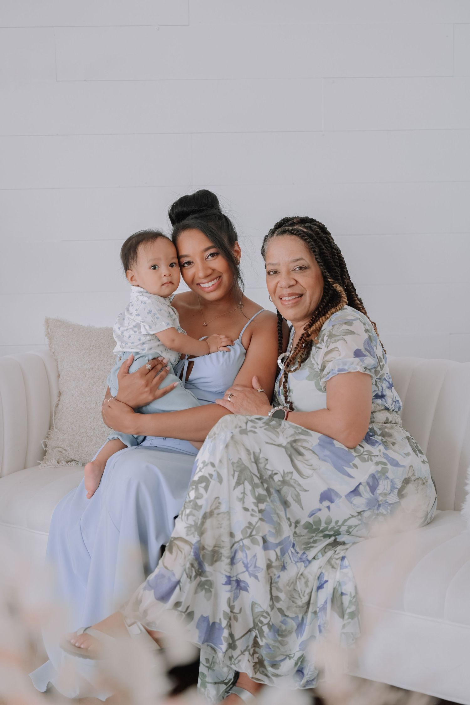 Three generations gather on white couch for intimate family portrait in matching pastel outfits.