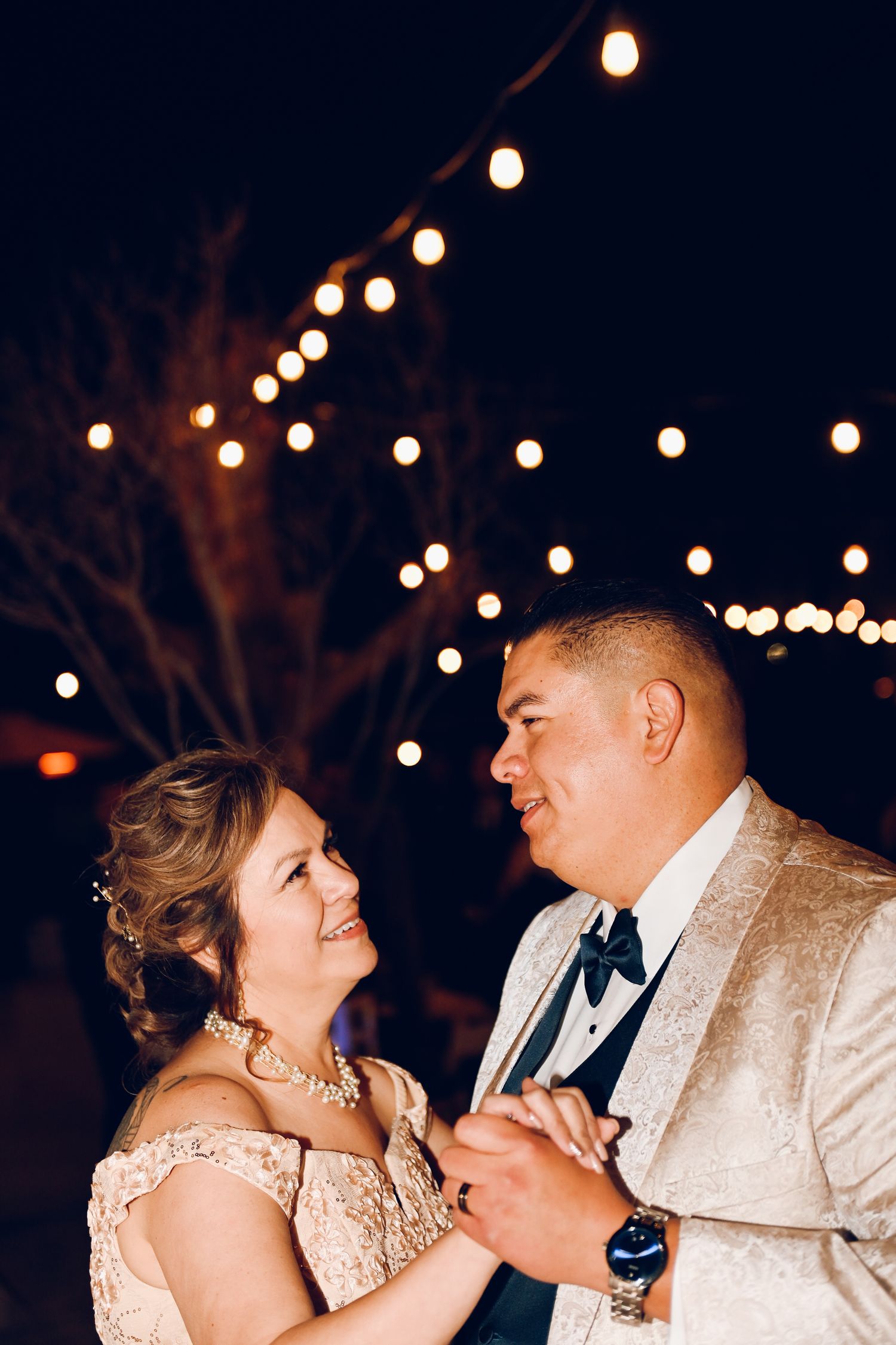 A romantic dance moment under glowing string lights at an outdoor evening celebration.