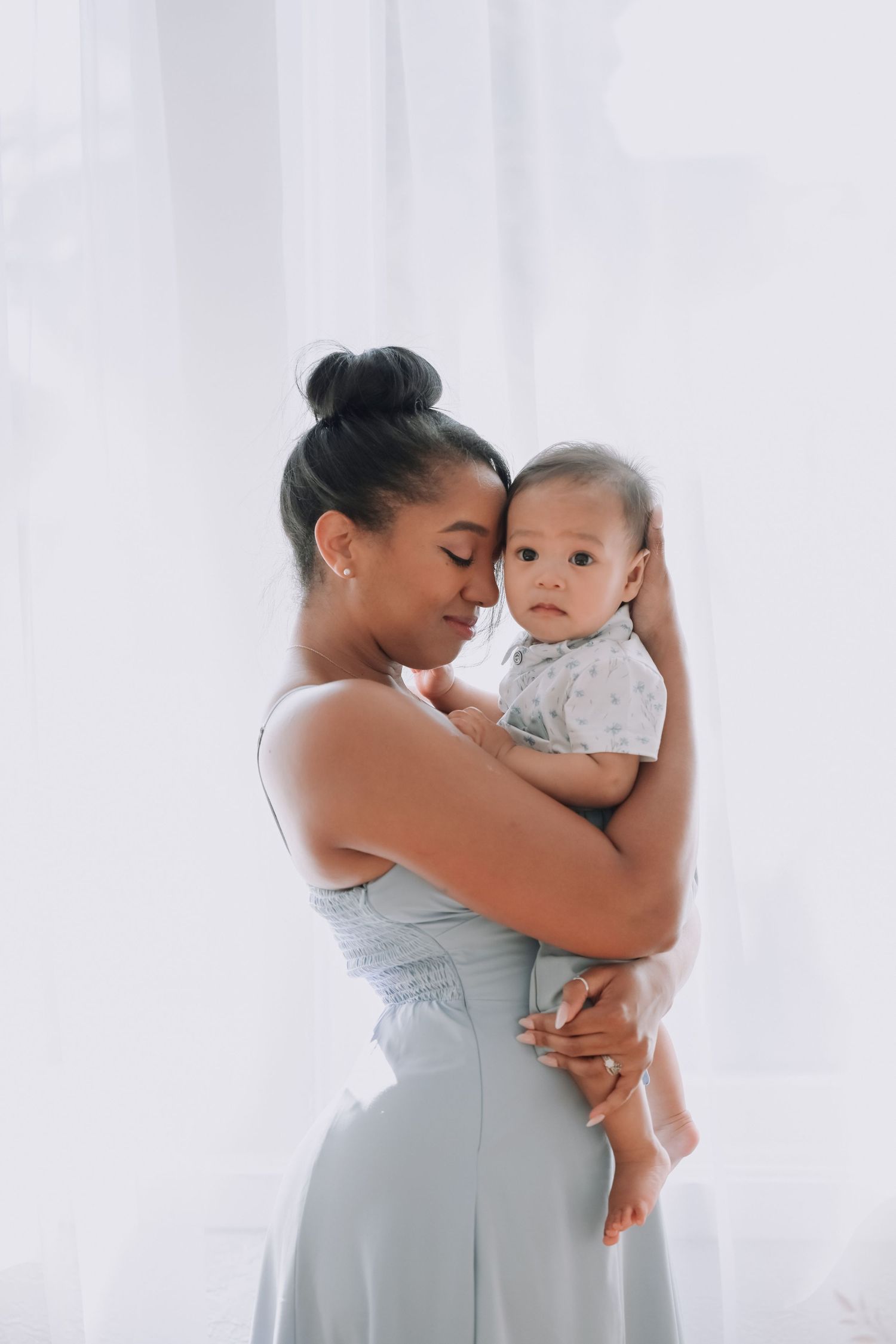 Tender moment captured between parent and baby in soft natural light against white background.