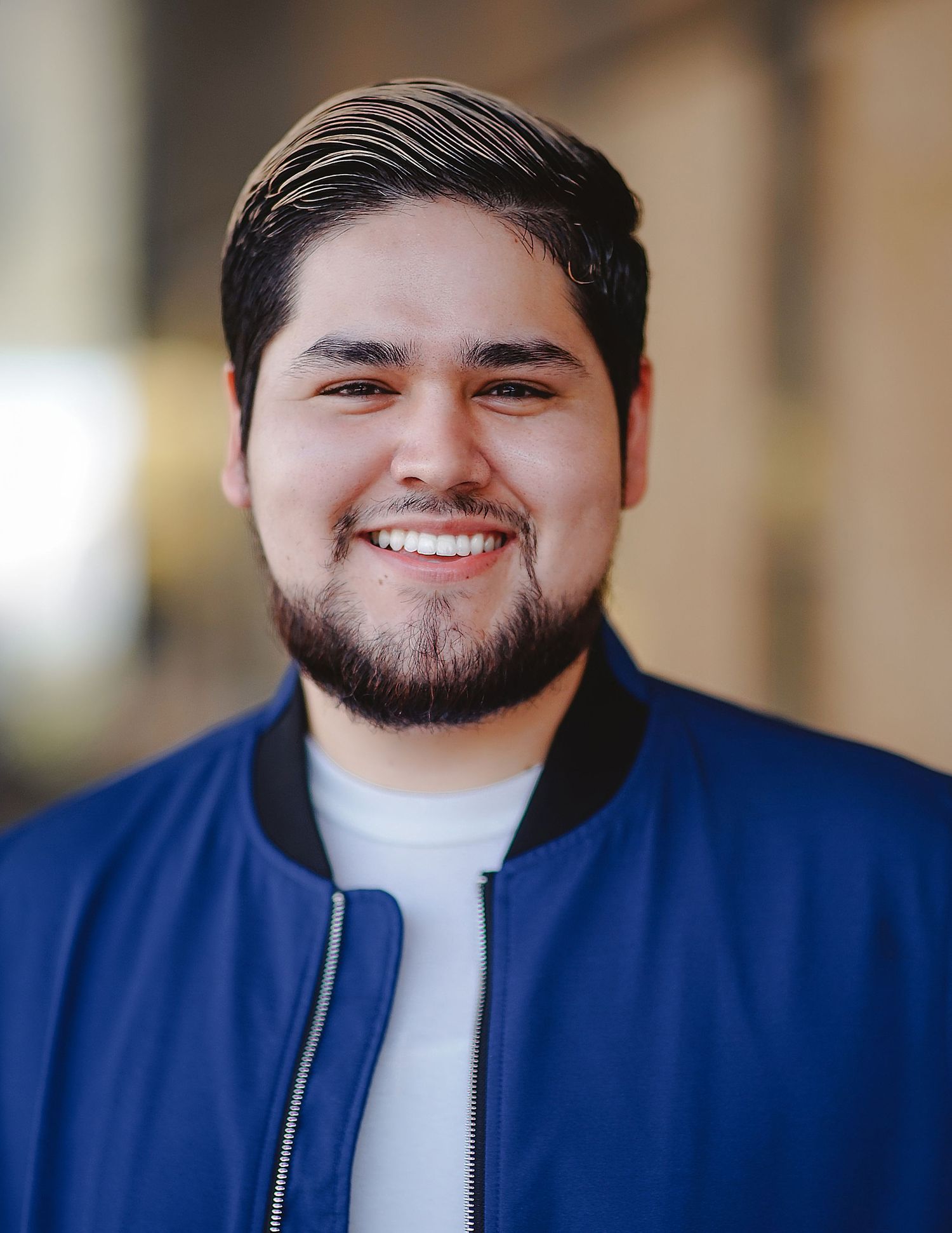 Professional headshot of person in blue jacket smiling warmly against blurred background.