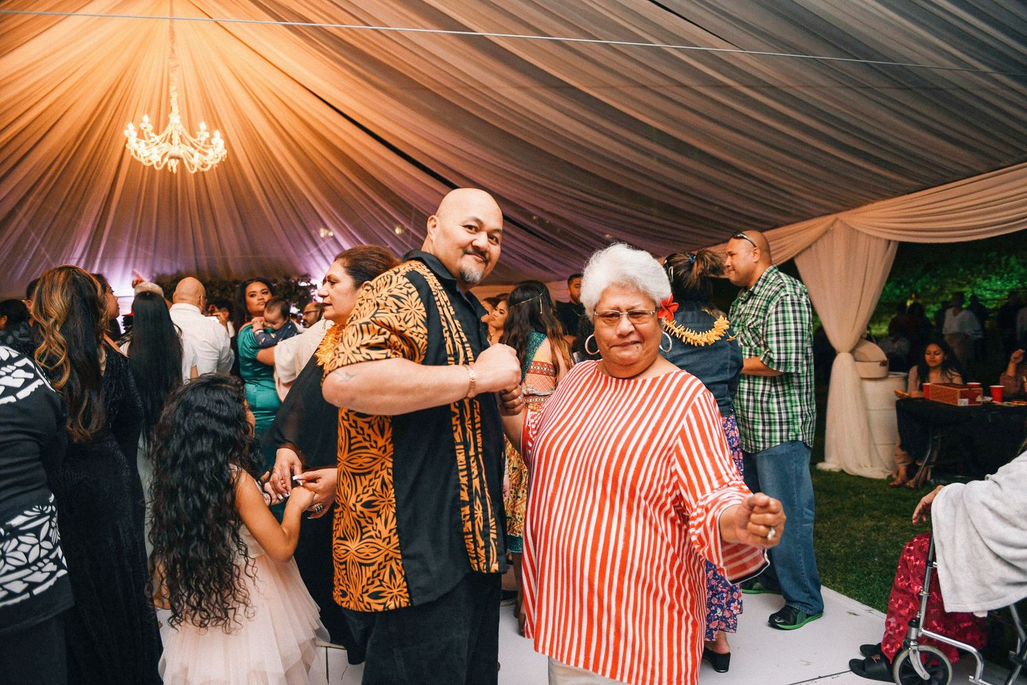 Wedding reception dance party under elegant draped tent with chandelier.
