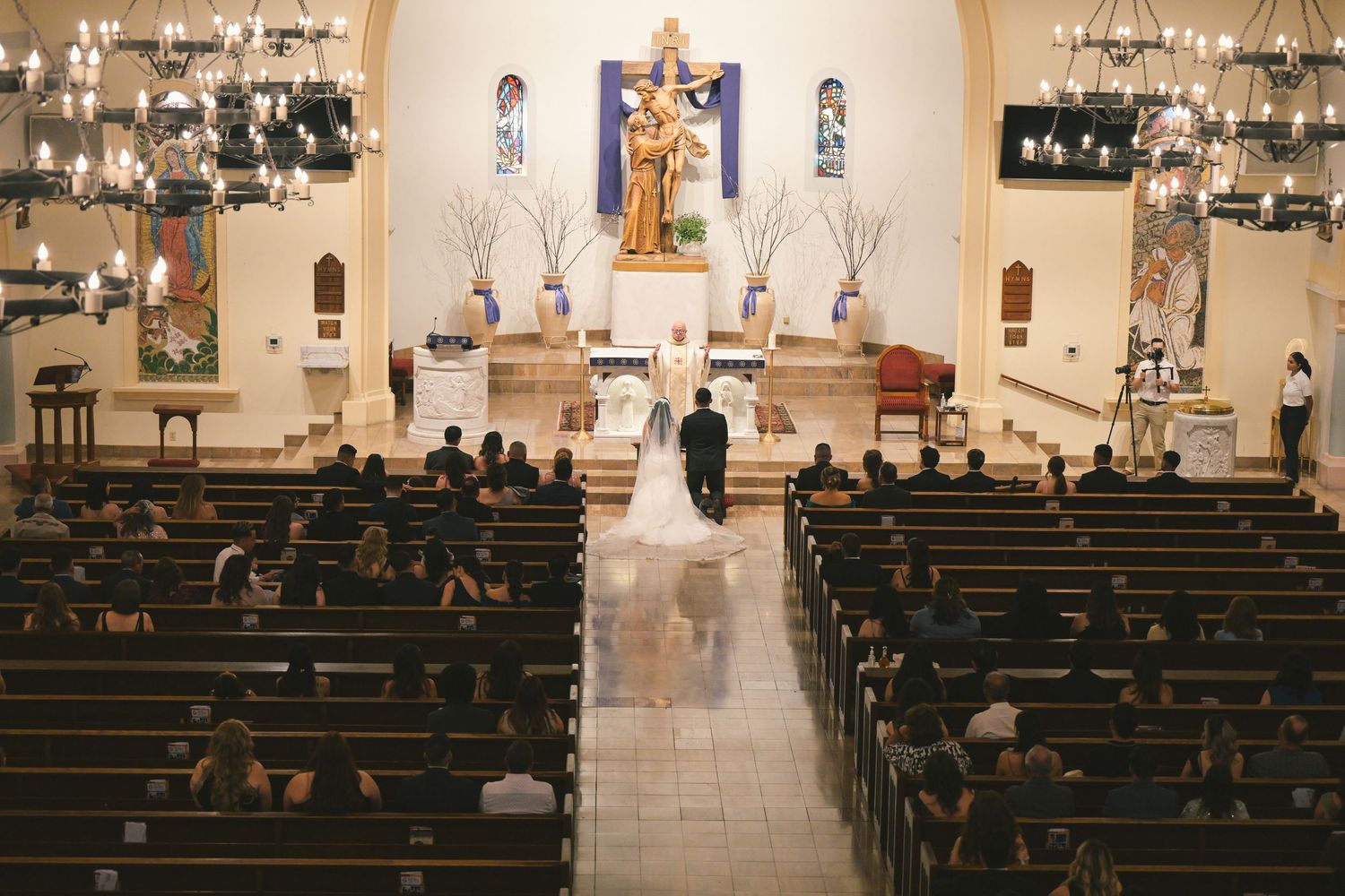 Catholic church wedding ceremony with ornate altar and religious statues.