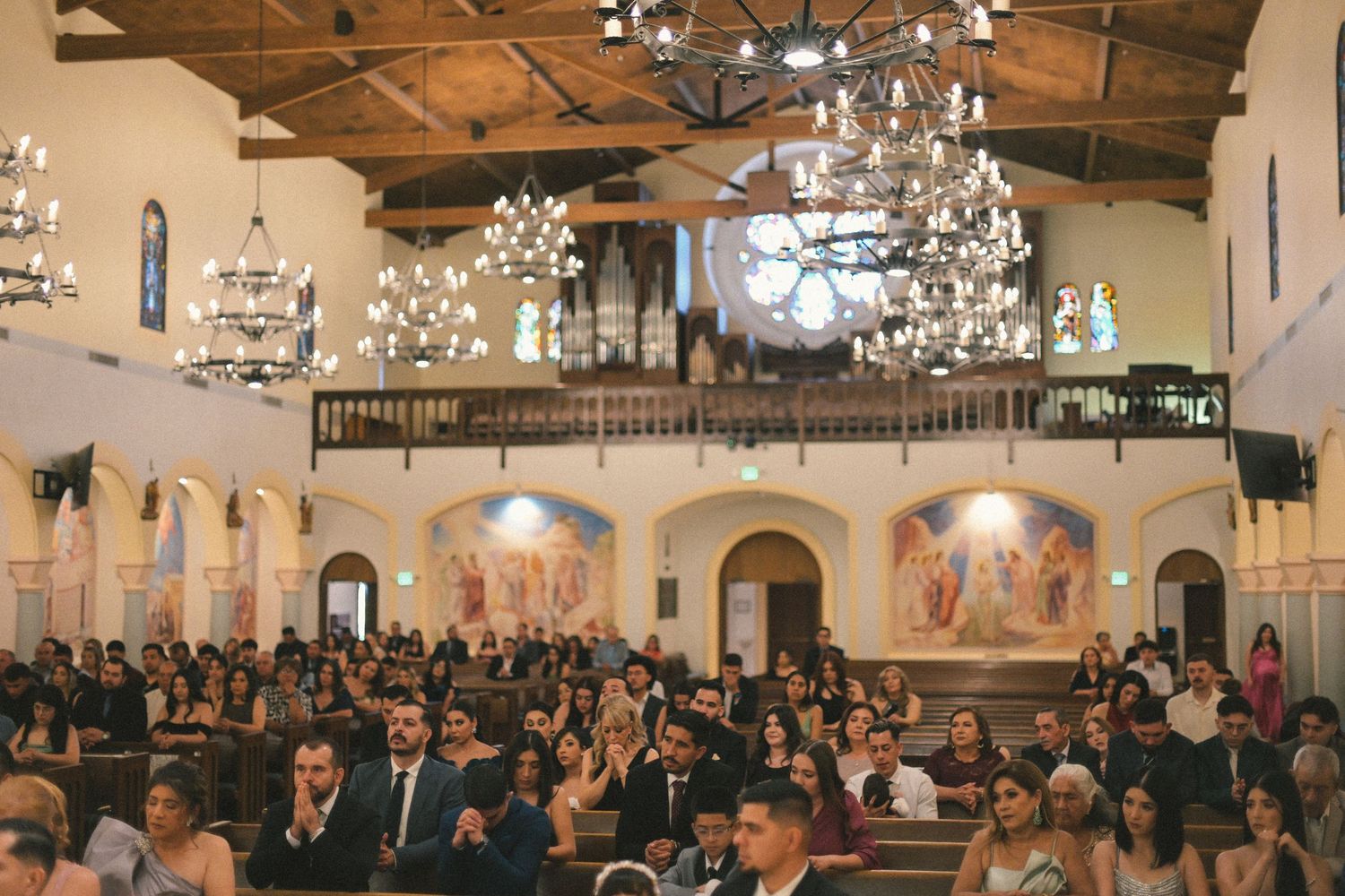 Interior of grand church filled with wedding guests under ornate chandeliers.