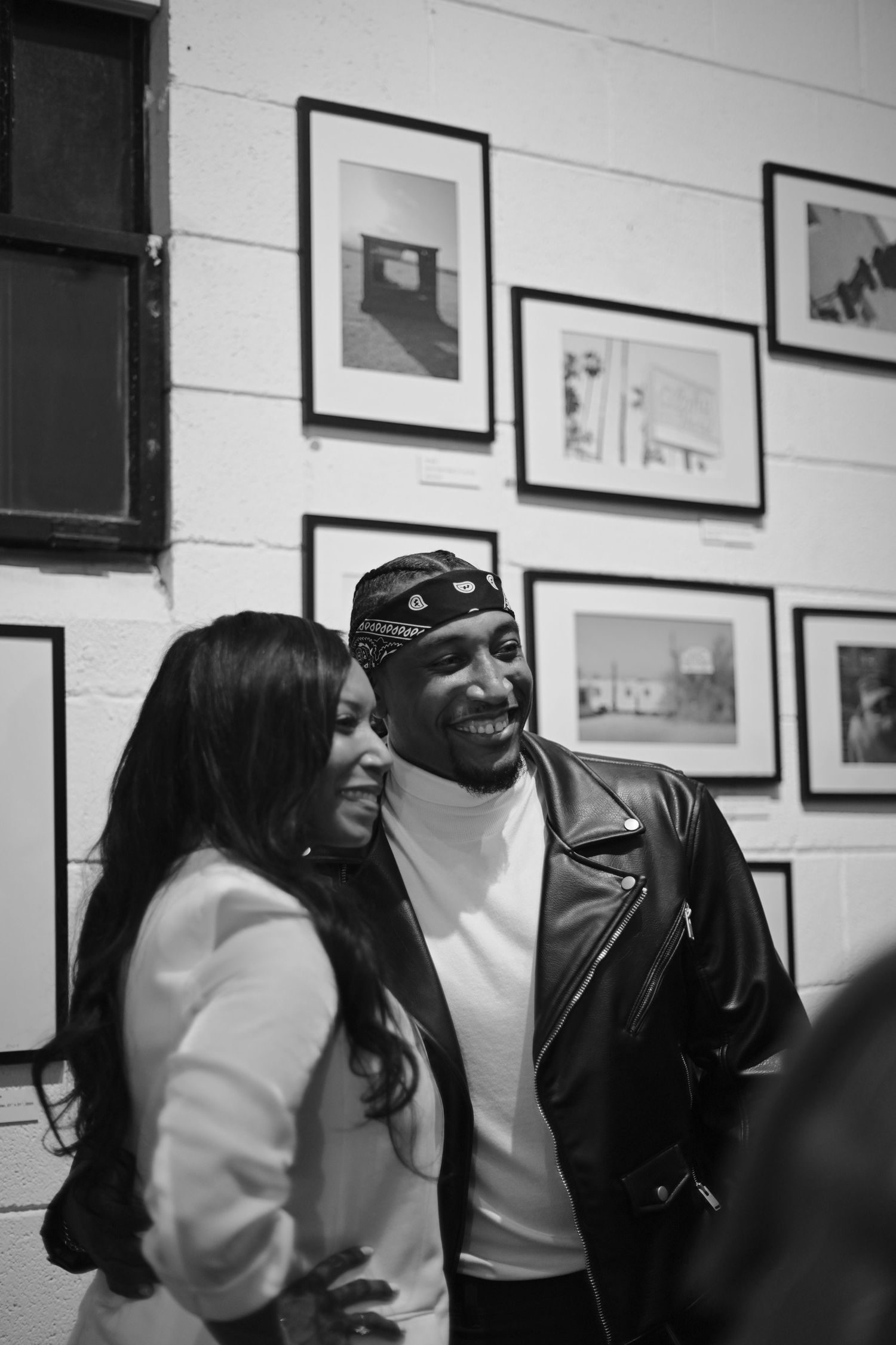 Two people share a candid moment against a white wall with framed artwork.