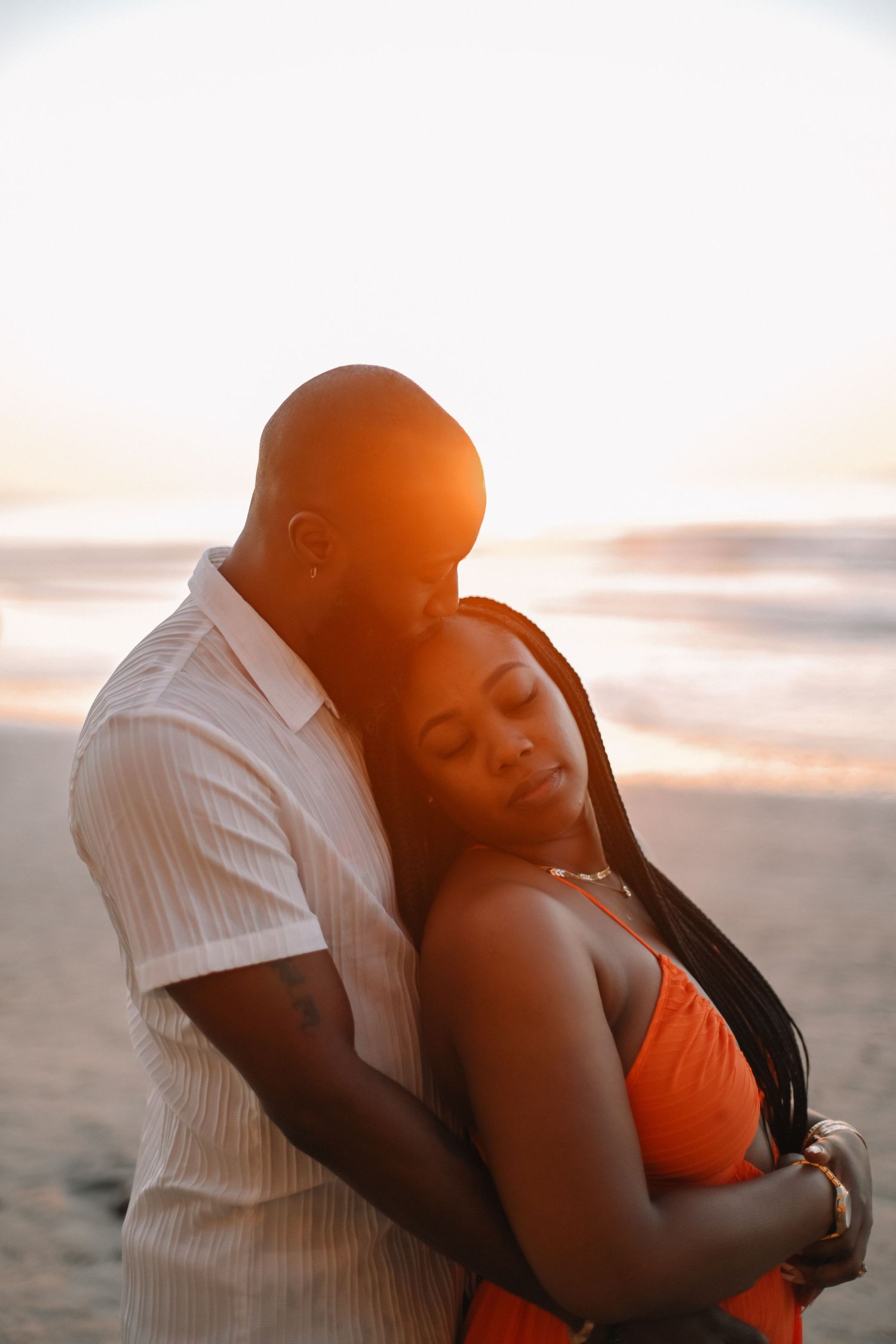 Romantic sunset beach portrait of couple embracing in white and orange attire.