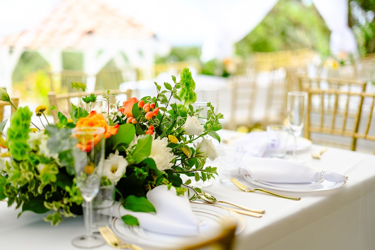 Elegant wedding table setting with fresh floral centerpiece featuring orange and white flowers with greenery.