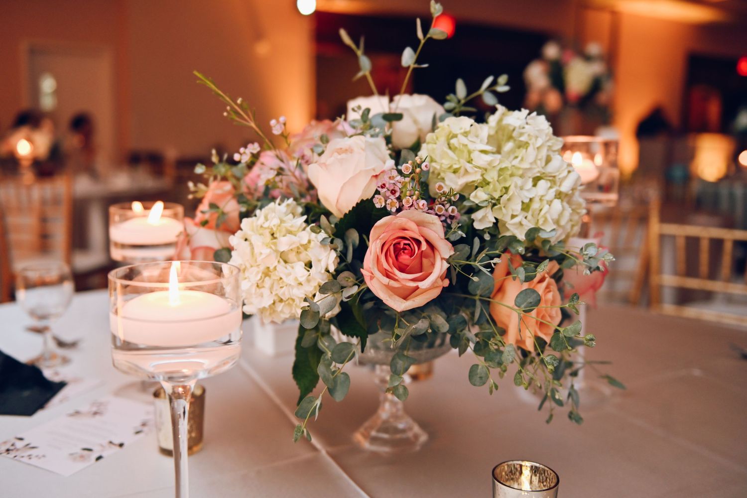 Elegant floral centerpiece with pink roses and white hydrangeas on wedding reception table.