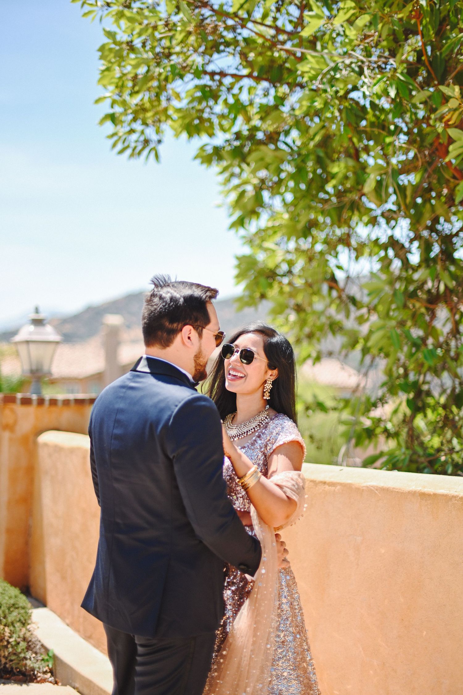 Romantic outdoor portrait of couple in formal attire against terracotta wall and palm trees.