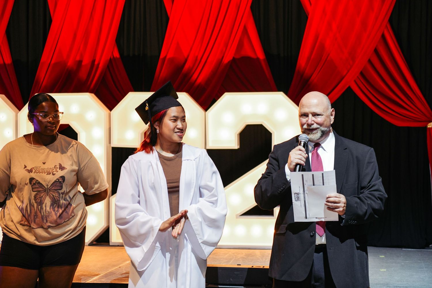 Stage presentation with red curtain backdrop featuring speakers at a formal ceremony.
