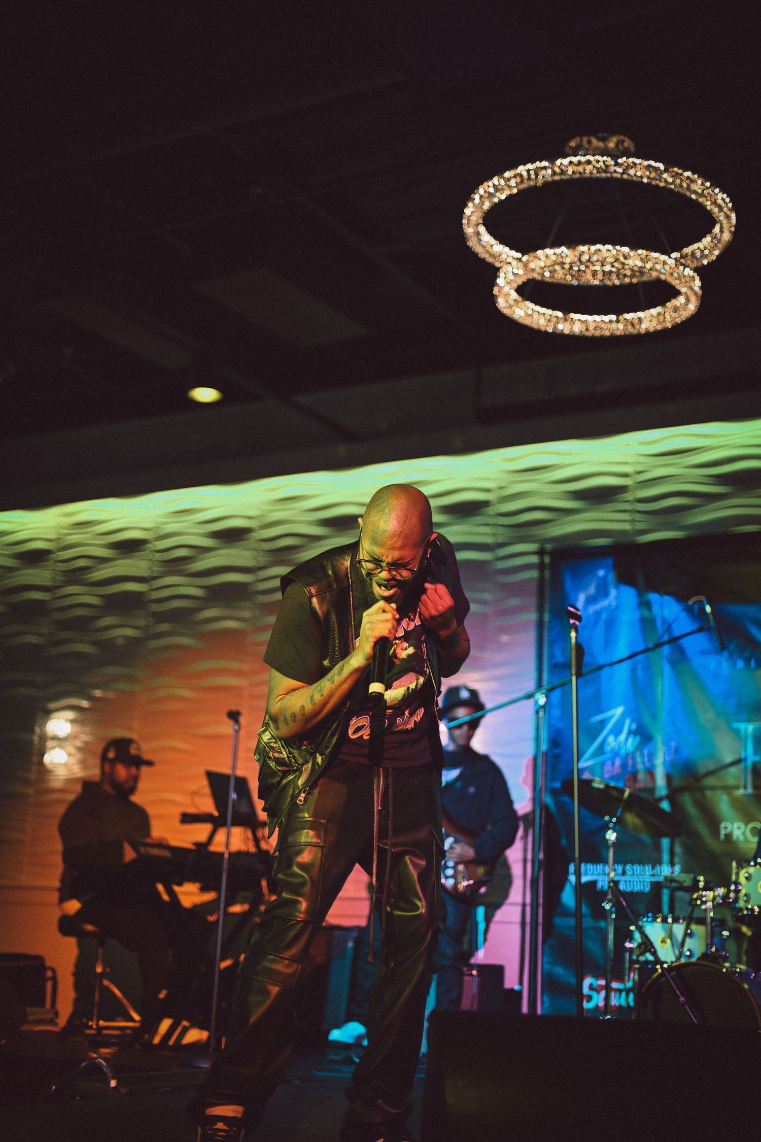 Singer performing on stage with band and decorative lighting rings above.