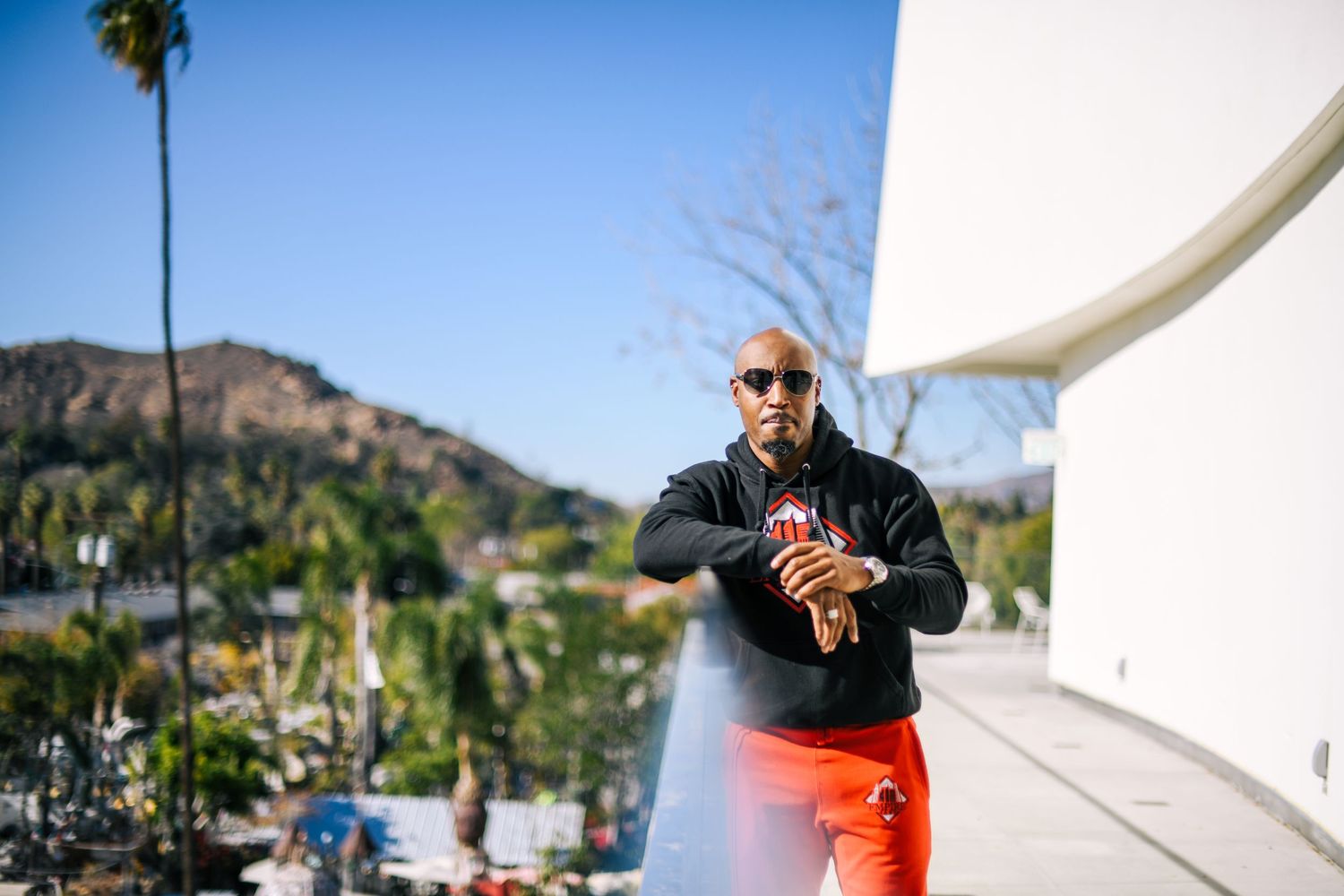 Person in black outfit checking time in sunny California setting with palm trees and mountains.