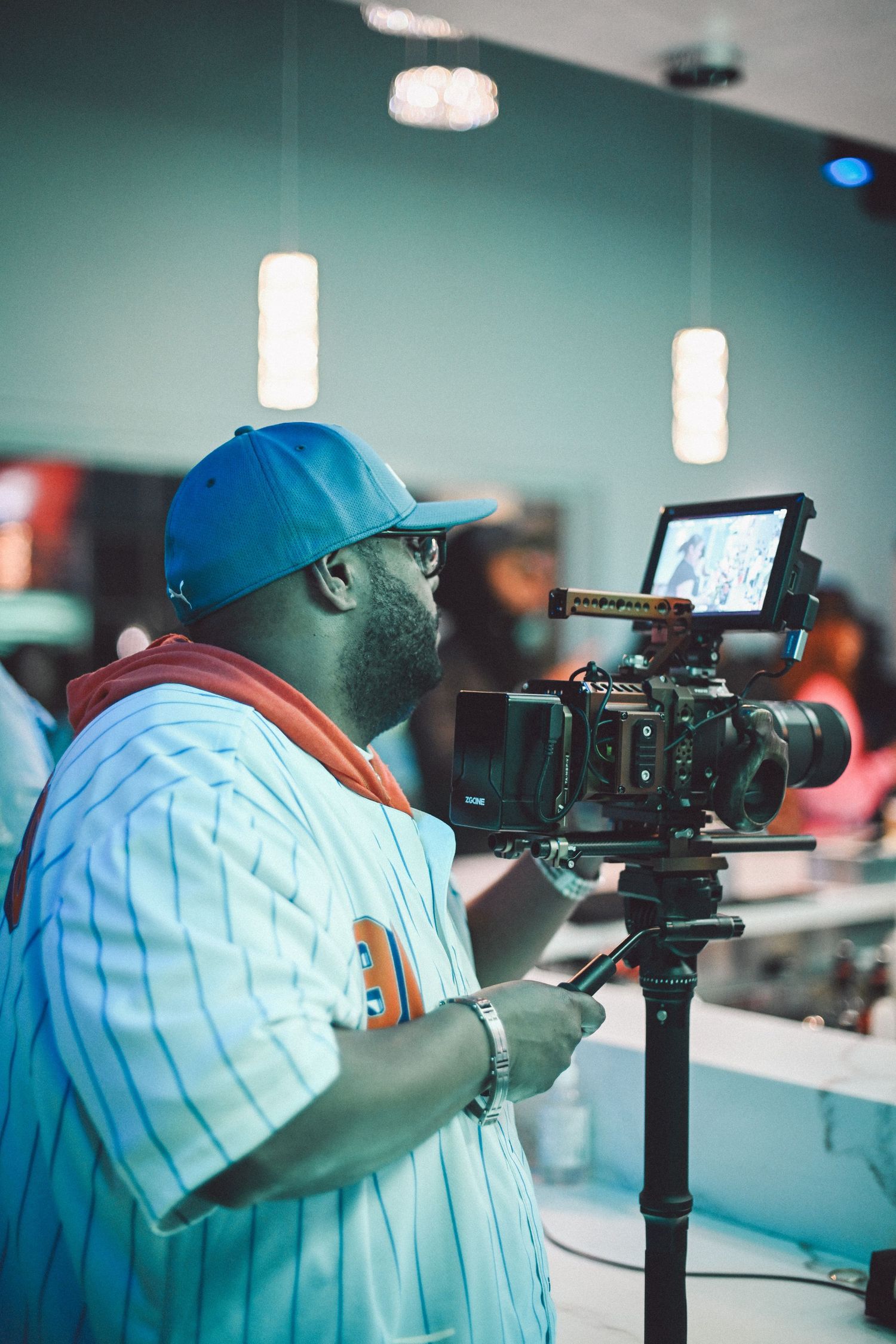 Cinematographer in a blue baseball cap operating a professional camera on set.