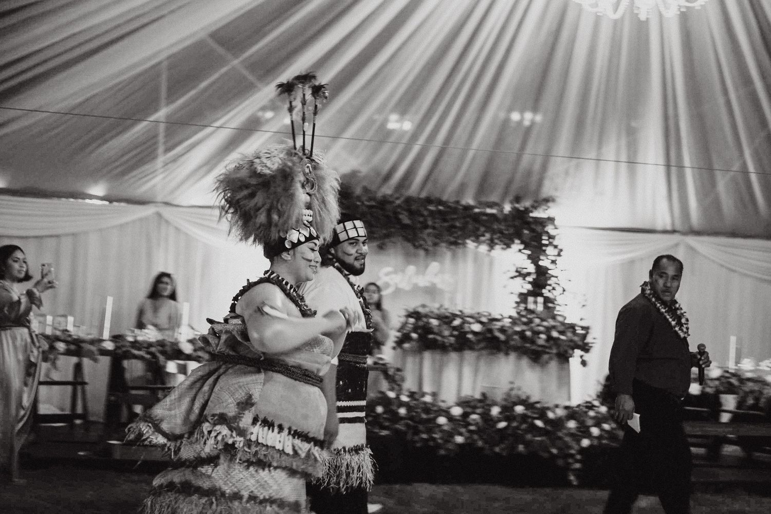 Black and white photo of traditional Polynesian dance performance in a decorated wedding tent.