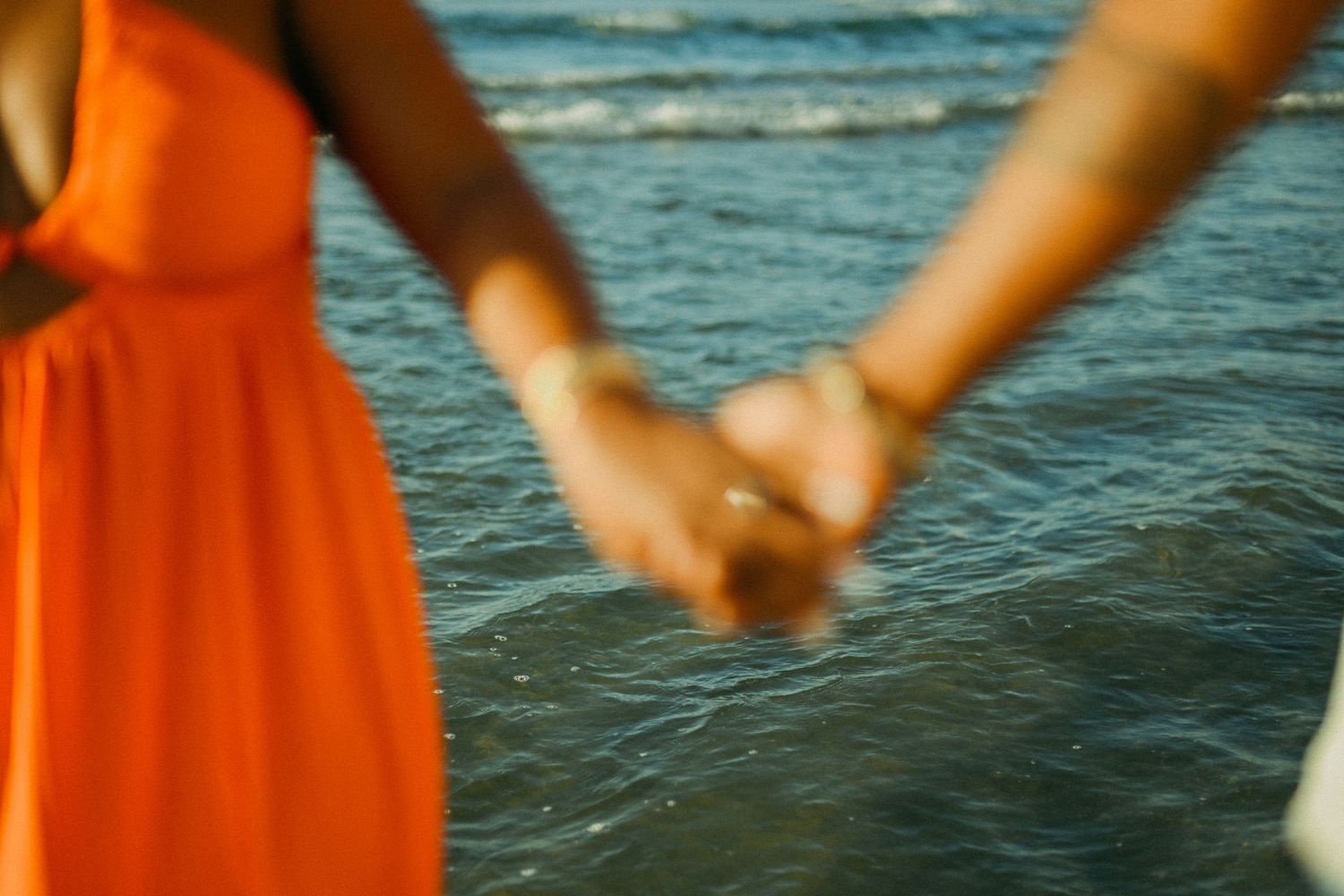 Close-up of couple holding hands against ocean waves at sunset.