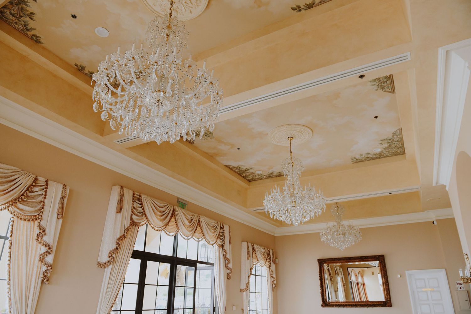 Elegant ballroom ceiling with ornate crystal chandeliers and detailed crown molding.