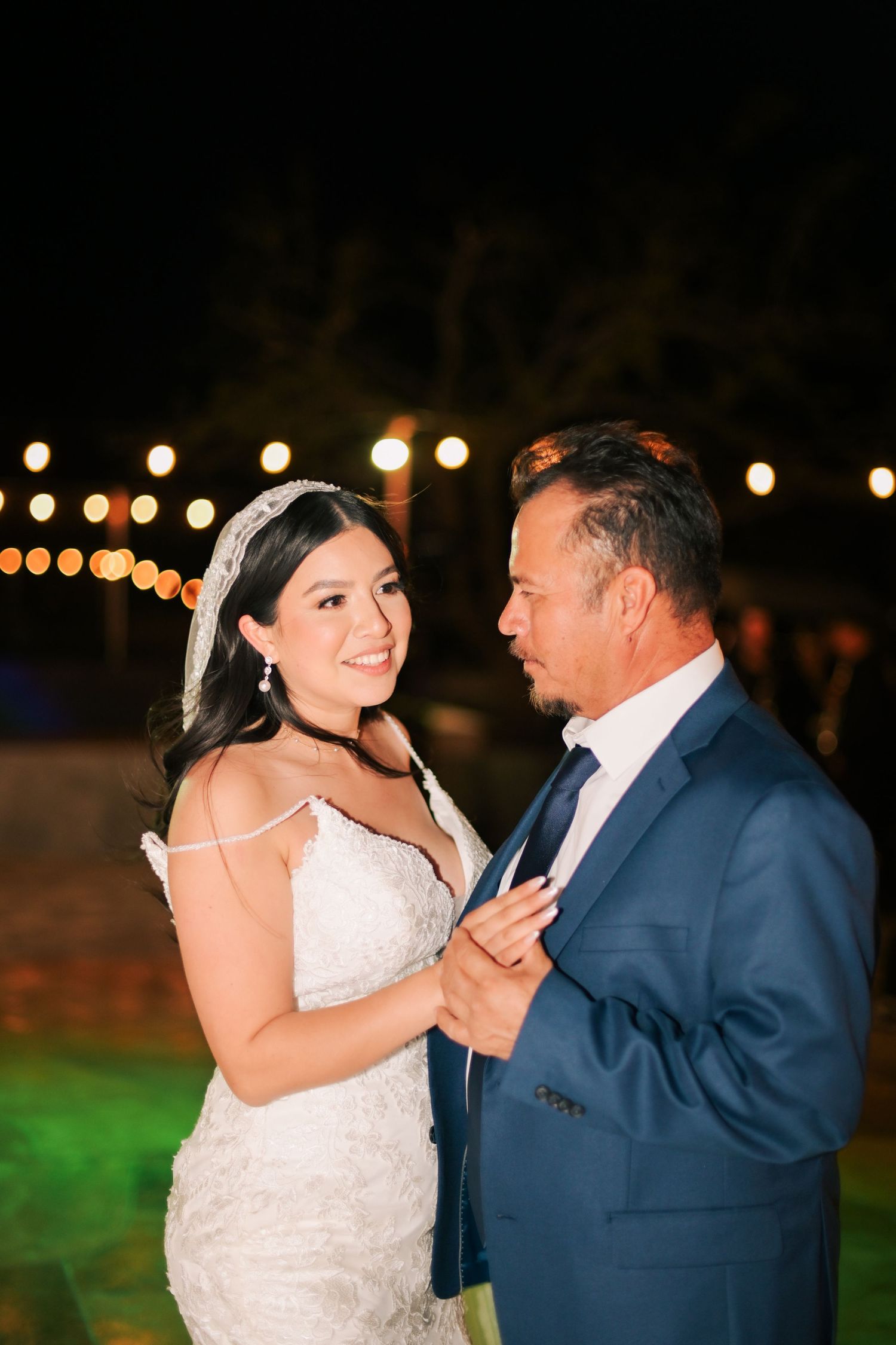 Couple shares intimate dance moment under twinkling outdoor lights at evening reception.