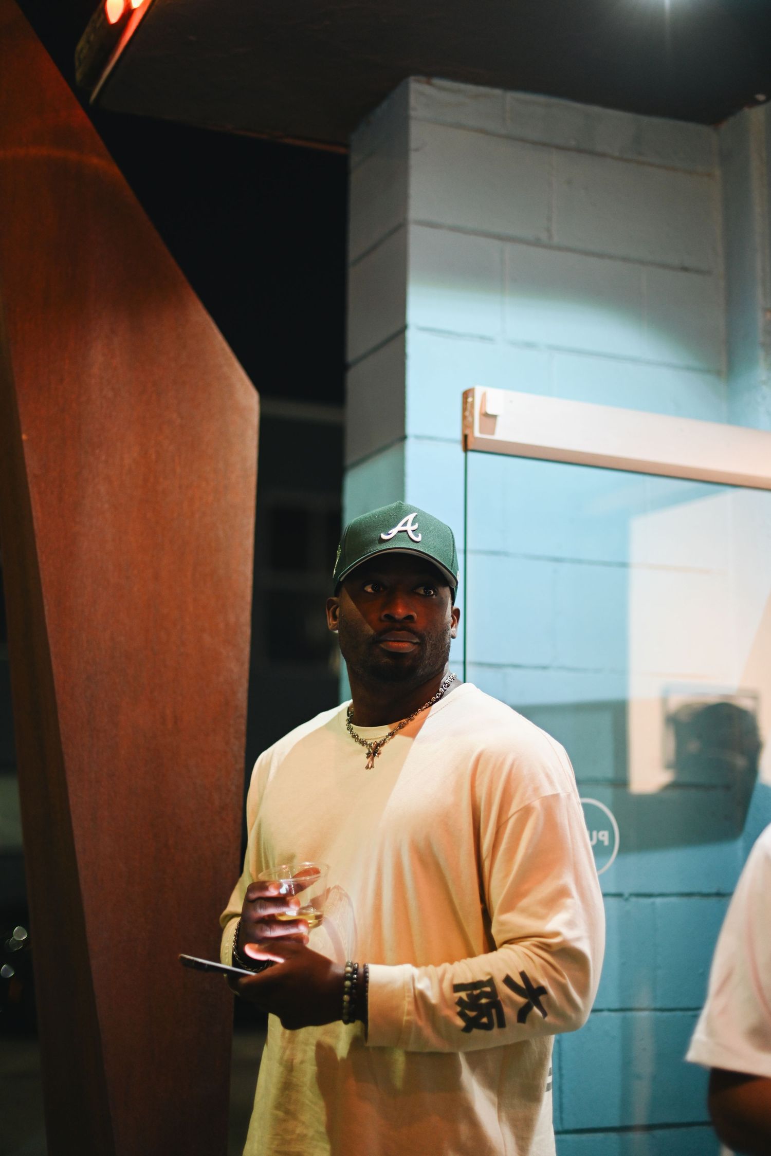 Person in casual attire stands against white wall wearing Atlanta baseball cap.