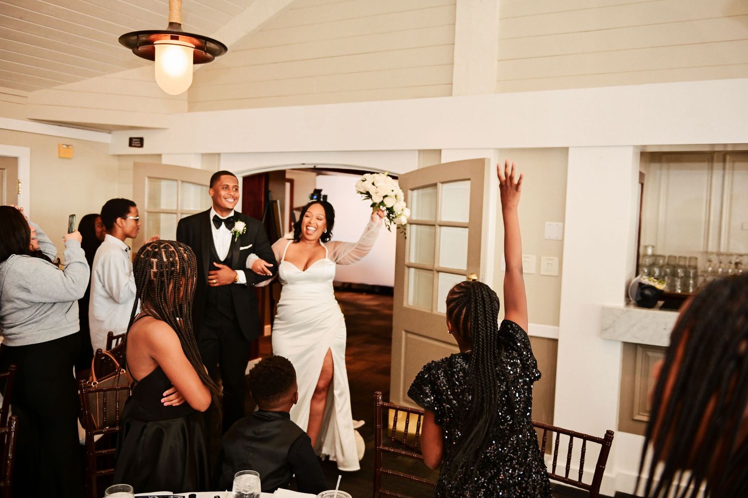Wedding guests celebrate during a reception with one person raising their hand in a joyful moment.