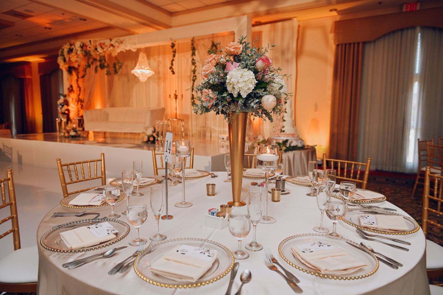 Formal wedding reception table with tall floral centerpiece and gold charger plates.