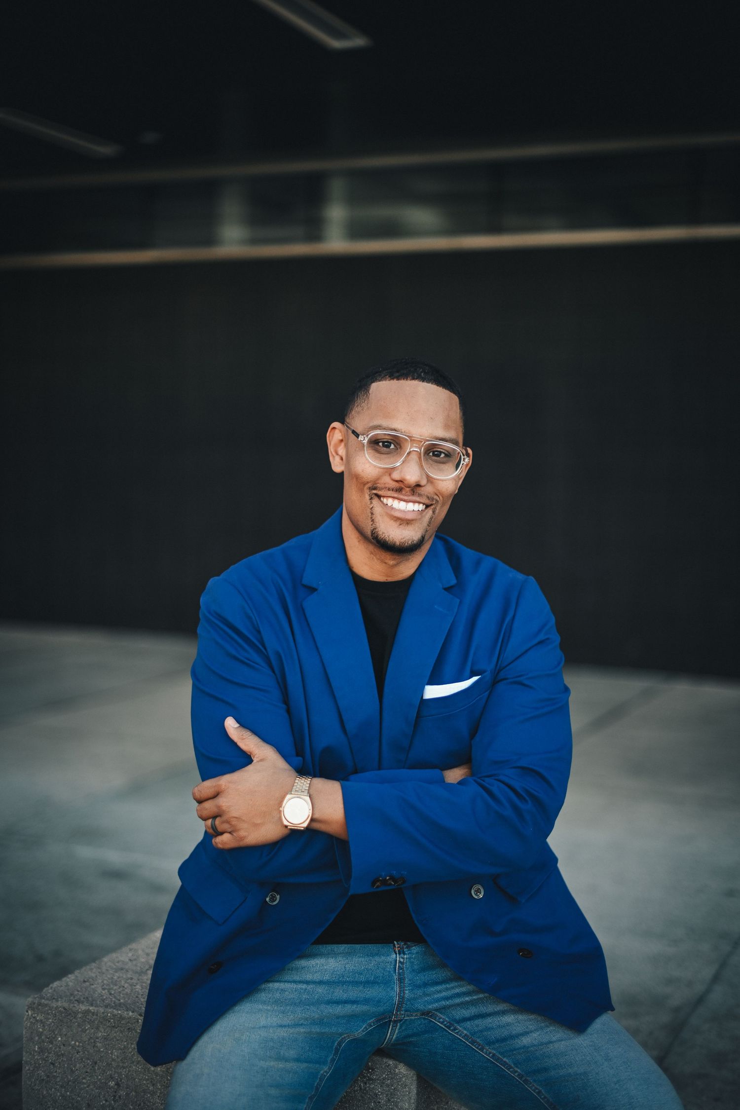 Person in bright blue blazer and glasses smiling confidently at camera.