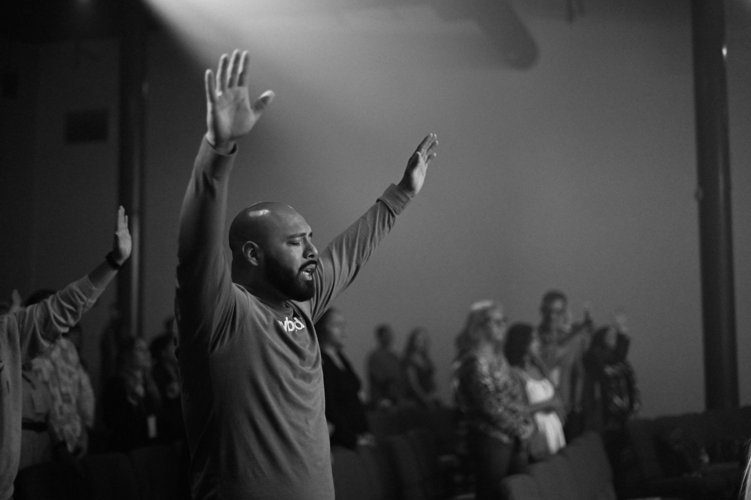 Black and white photo of person worshipping with raised hands during indoor service.