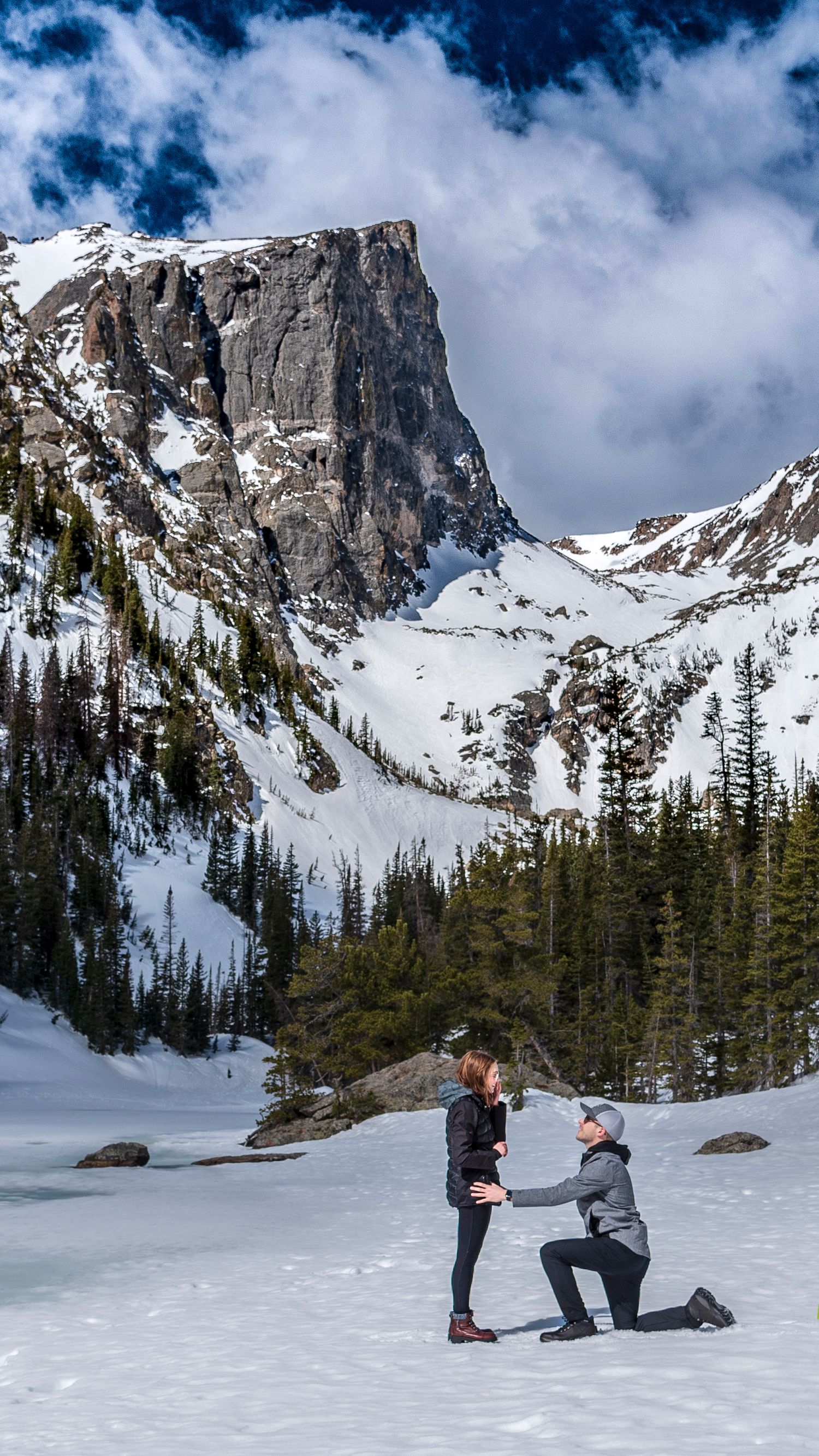 Man down on one knee at Dream Lake in Rocky Mountain National Park for a surprise marriage proposal captured by hidden photographer