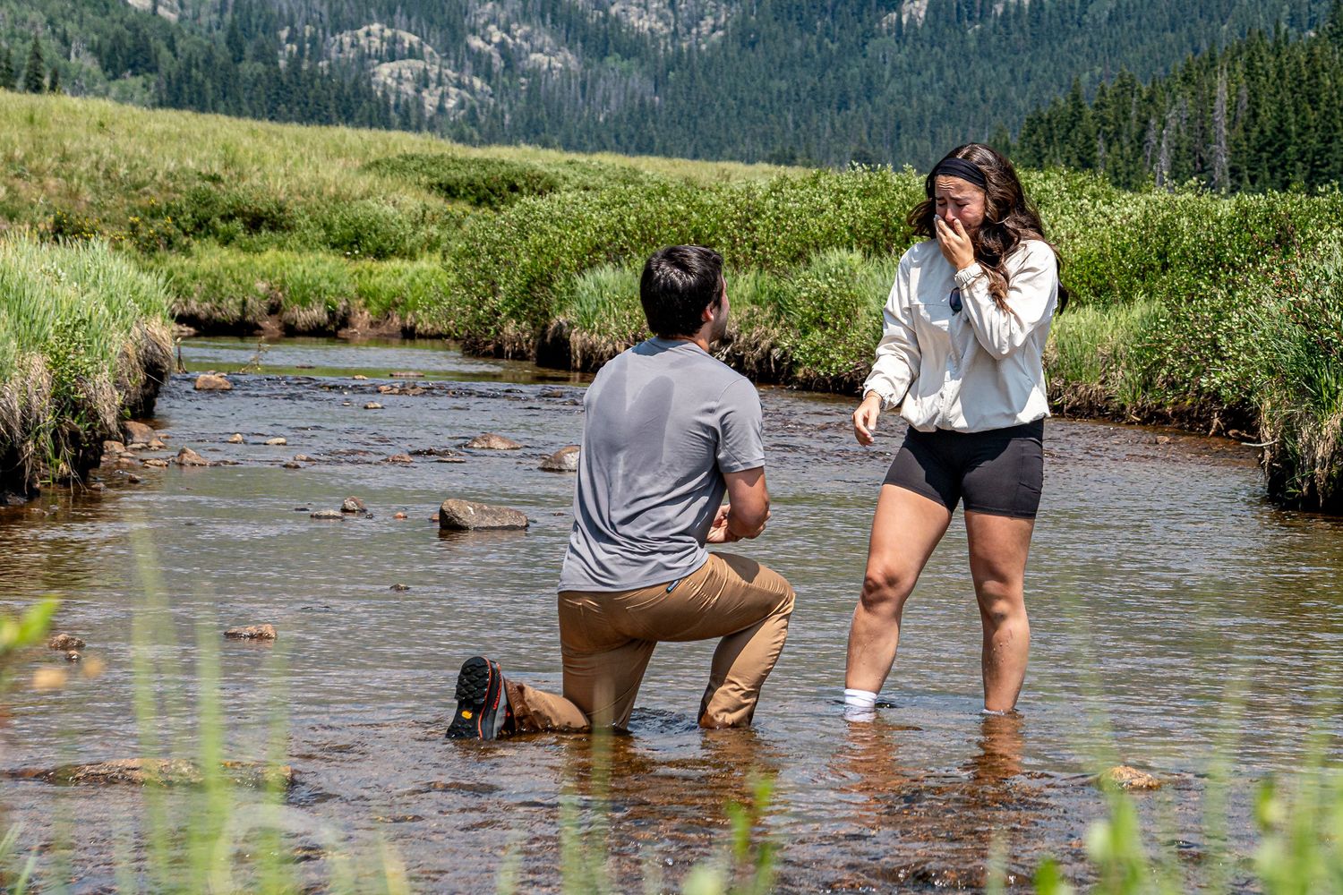Woman crying as her boyfriend is down on one knee in the middle of a river to propose to her near Vail, CO