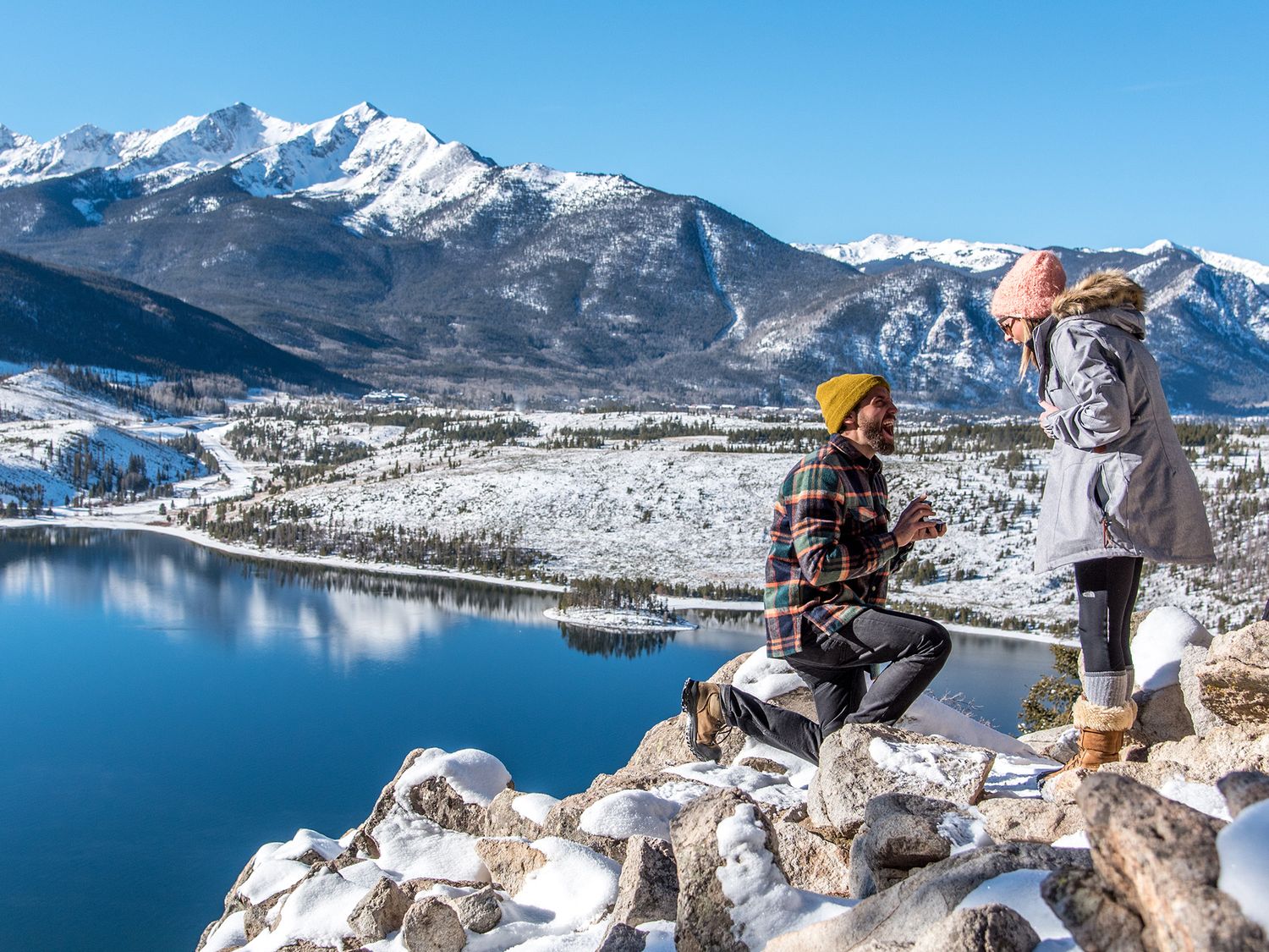 Man proposing at Sapphire Point Overlook in Breckenridge, Colorado with snow-covered mountains and Dillon Reservoir in the background during
