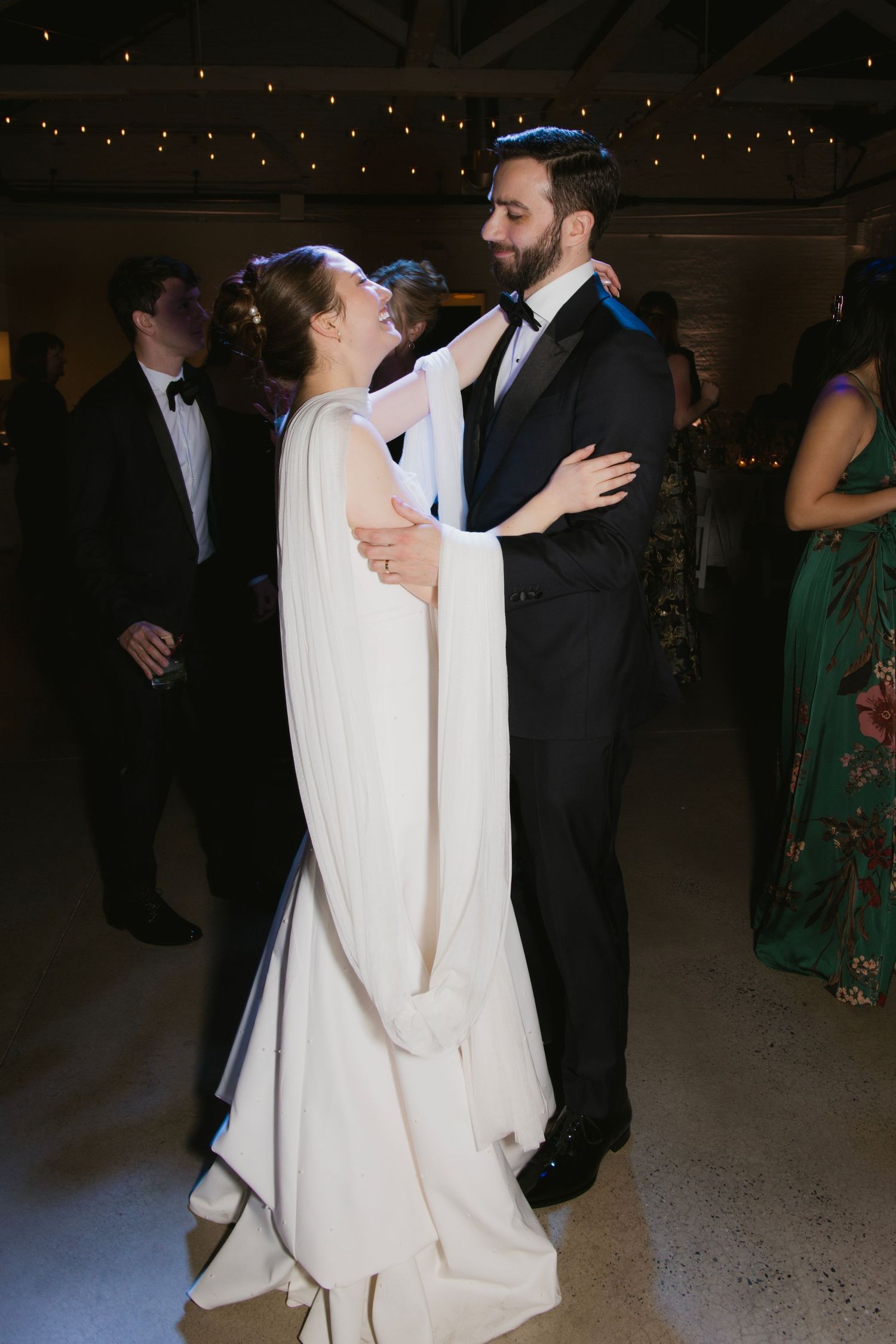 A romantic first dance moment at an evening wedding reception with twinkling lights in the background.