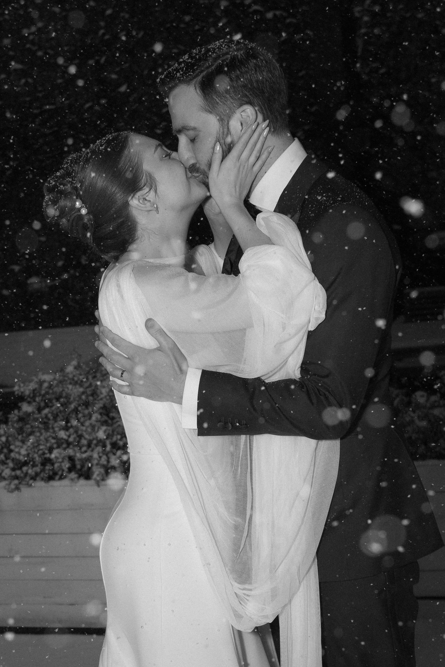 A romantic winter wedding dance captured in black and white with snowflakes falling.