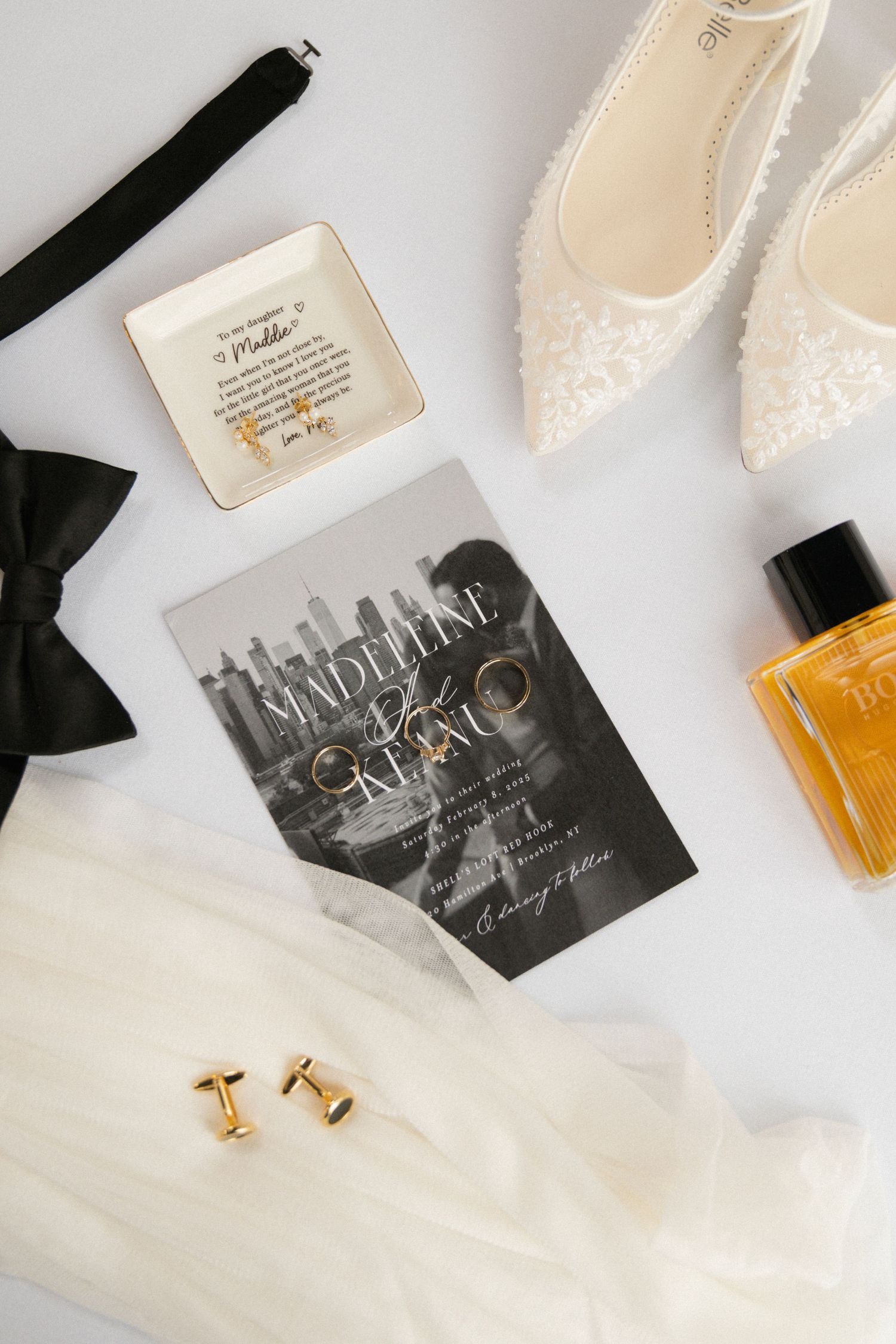 Flat lay of wedding accessories including invitation, shoes, bow tie and jewelry.