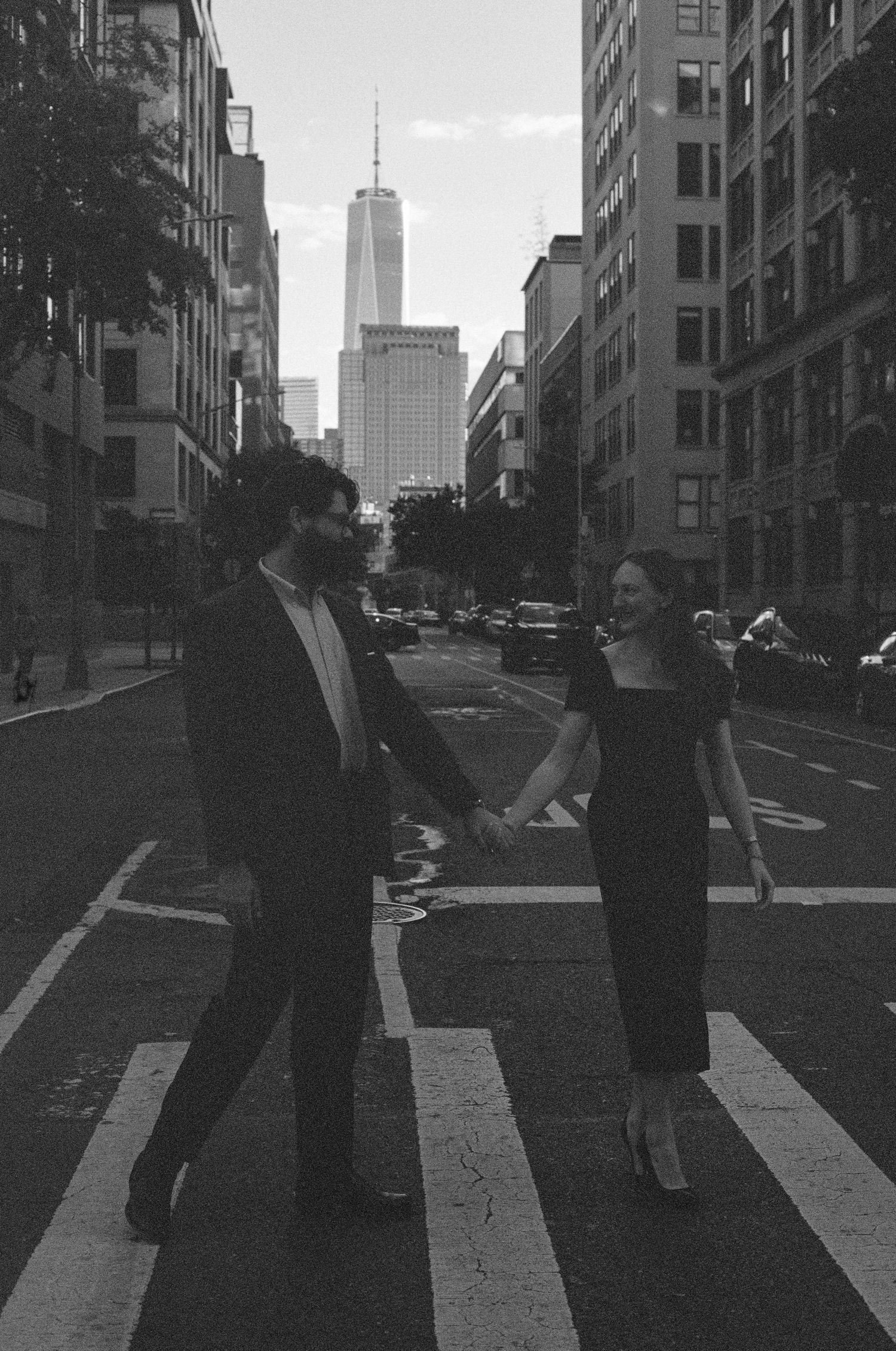 Black and white photo of couple on city street with Freedom Tower visible in background.