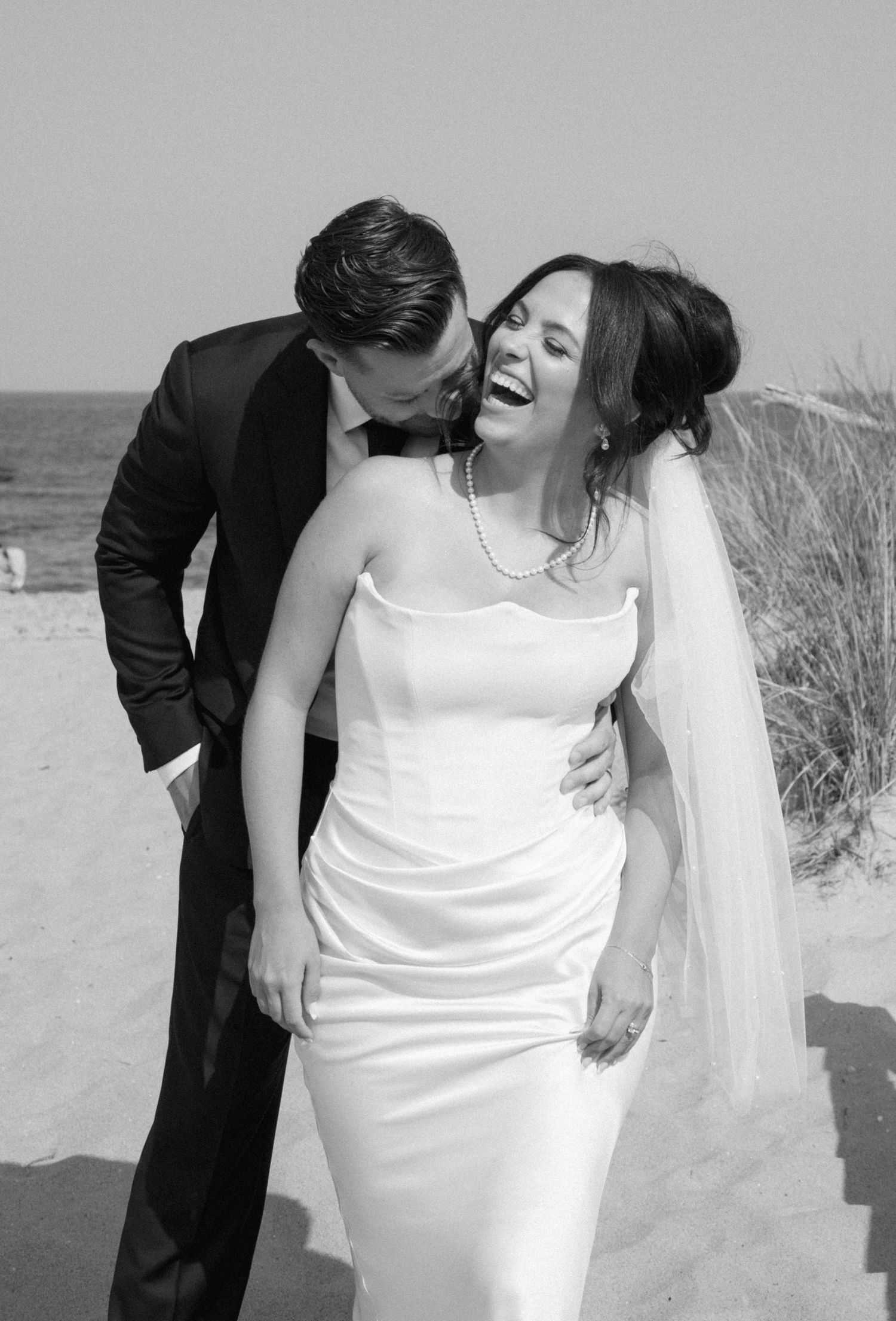 A romantic black and white sequence of a newlywed couple kissing and dancing on a beach.