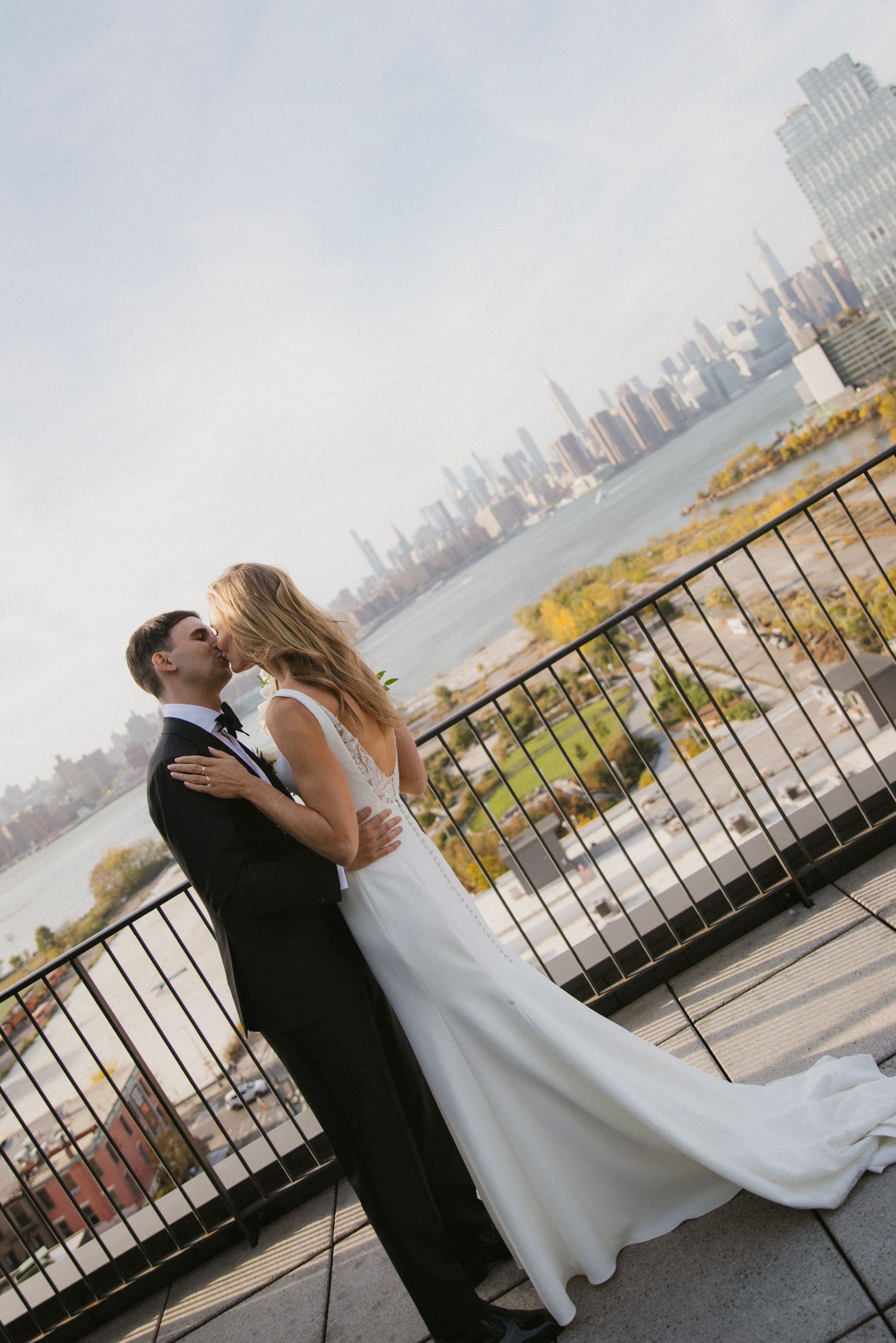 A couple in wedding attire embracing on a rooftop terrace with city skyline in background.