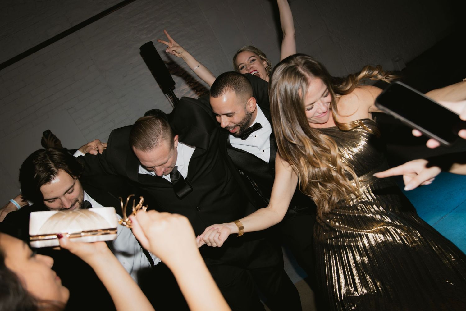 Wedding guests dancing energetically on a dark dance floor during reception celebrations.