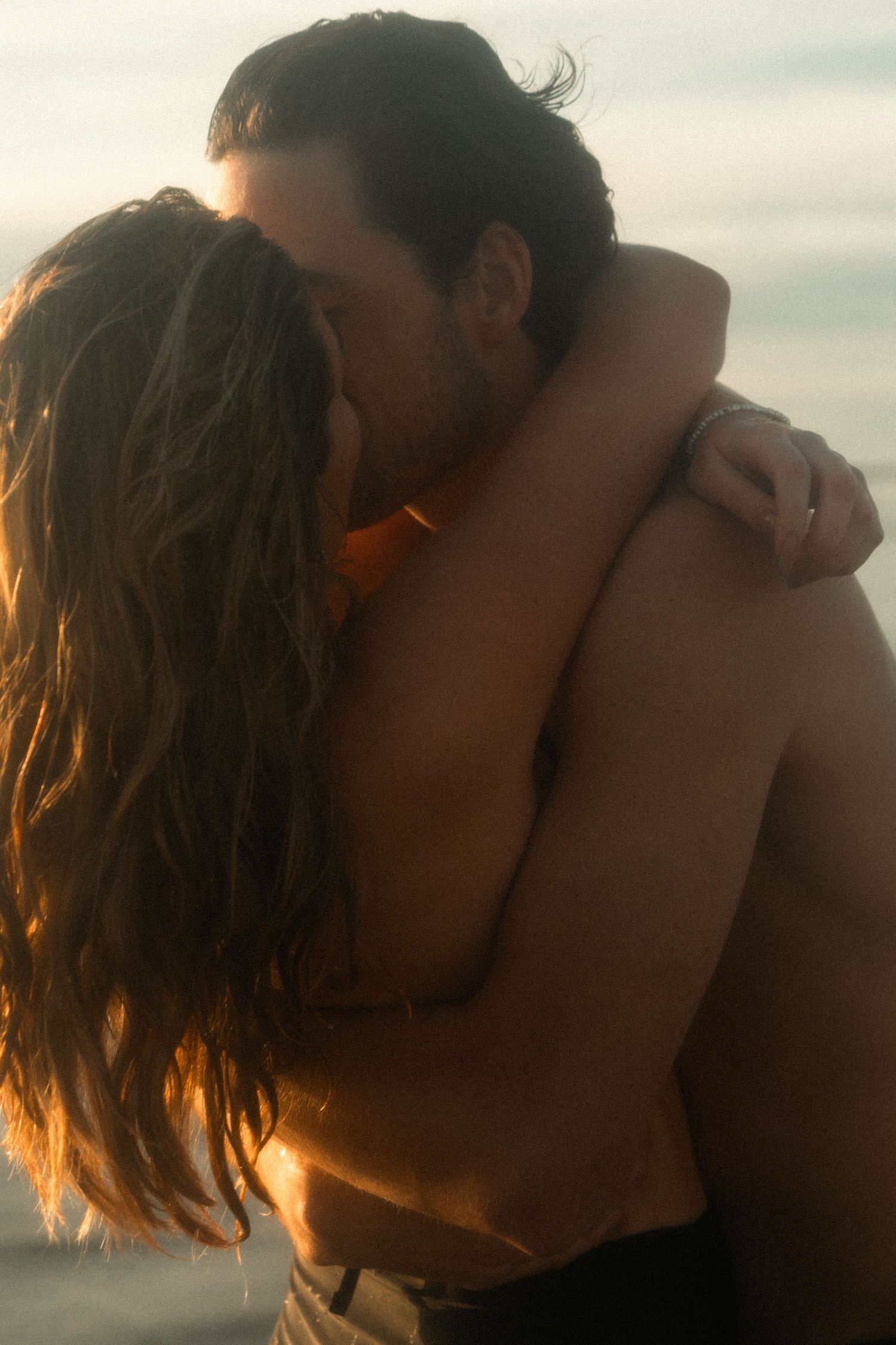 A romantic silhouette of a couple embracing at sunset with golden sunlight illuminating their intimate moment.
